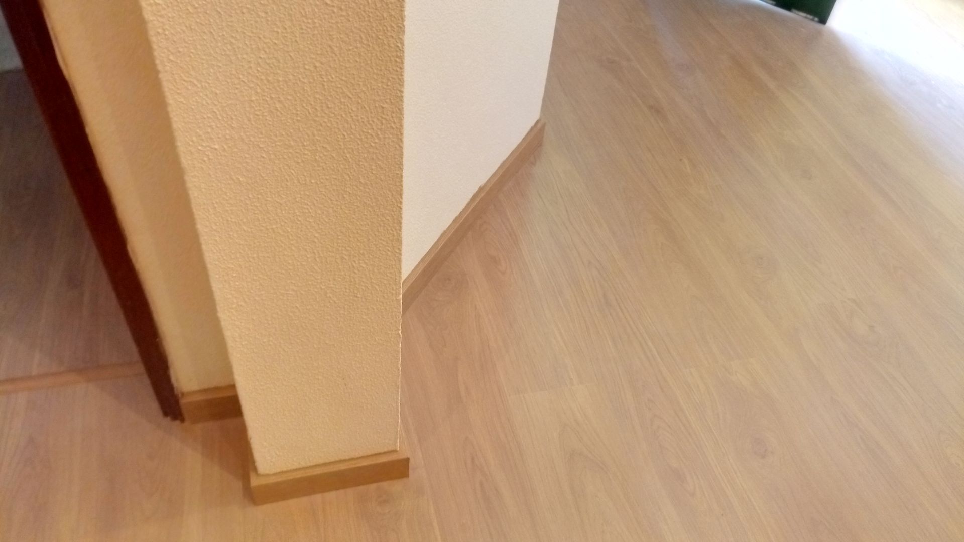 Piso de madeira e paredes bege em um quarto, com um vislumbre de uma porta marrom à esquerda.