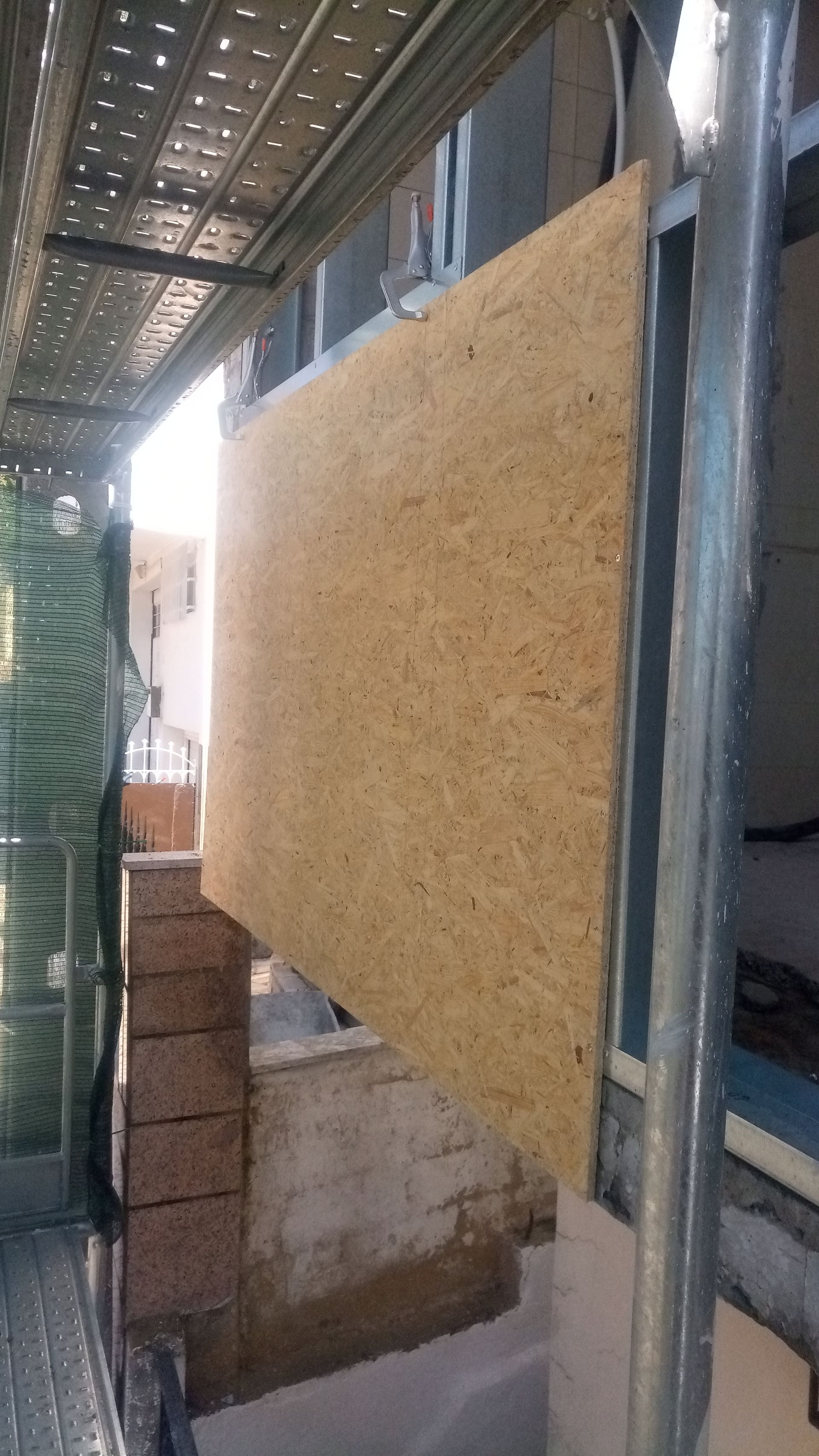 Placa de OSB instalada na parte externa do edifício, adjacente ao andaime e à alvenaria.