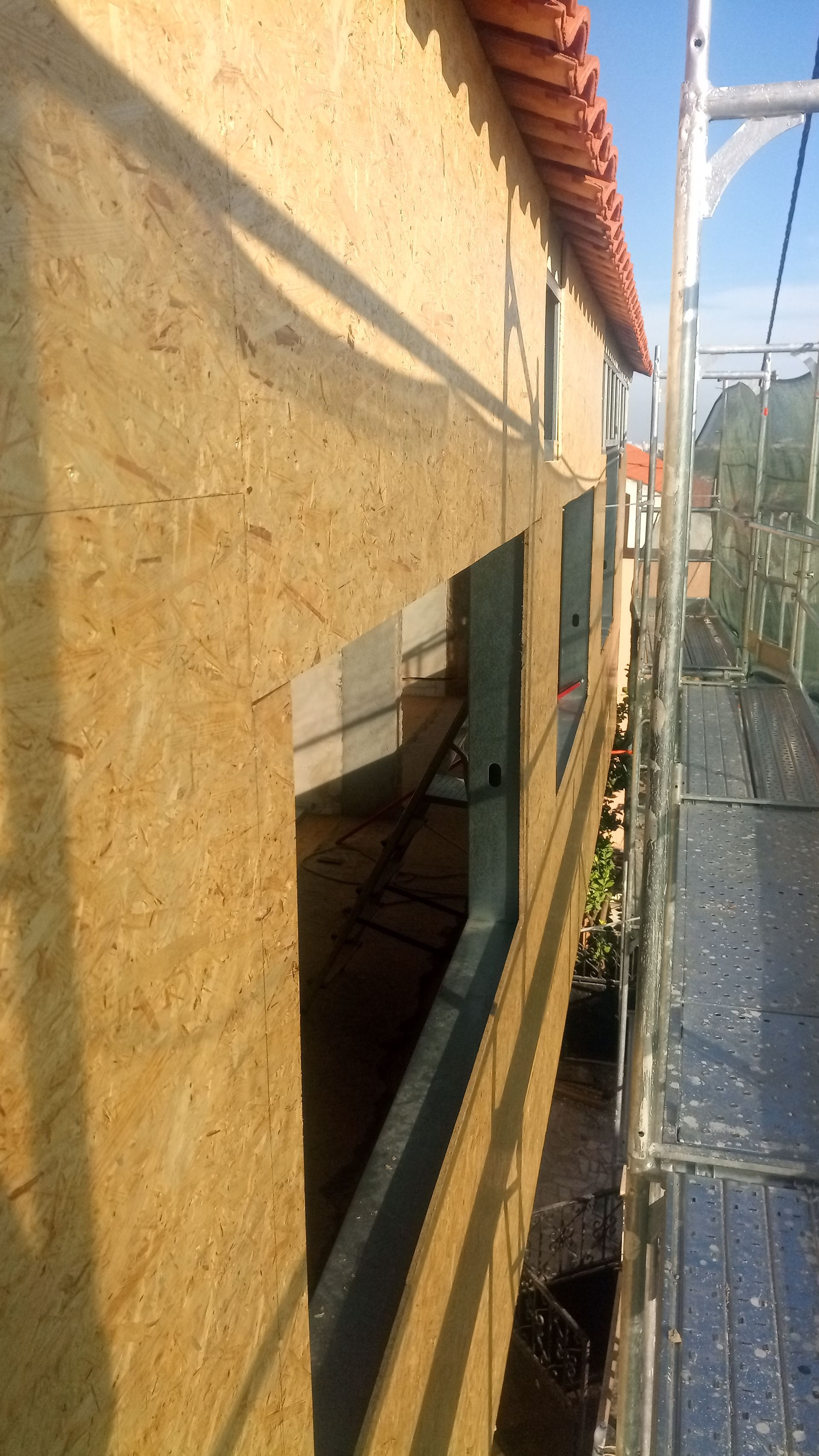 Construção da parede externa com painéis OSB (Oriented Strand Board), aberturas para janelas, andaimes e telhado de telha vermelha.