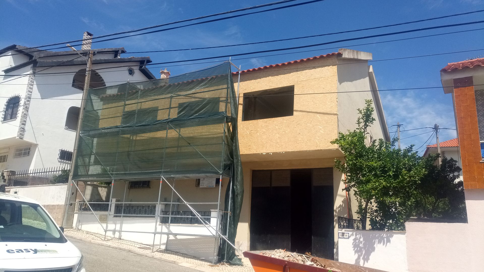 Prédio de dois andares em reforma; andaimes cobertos com tela verde. Fachada em amarelo vivo e branco, telhado marrom.