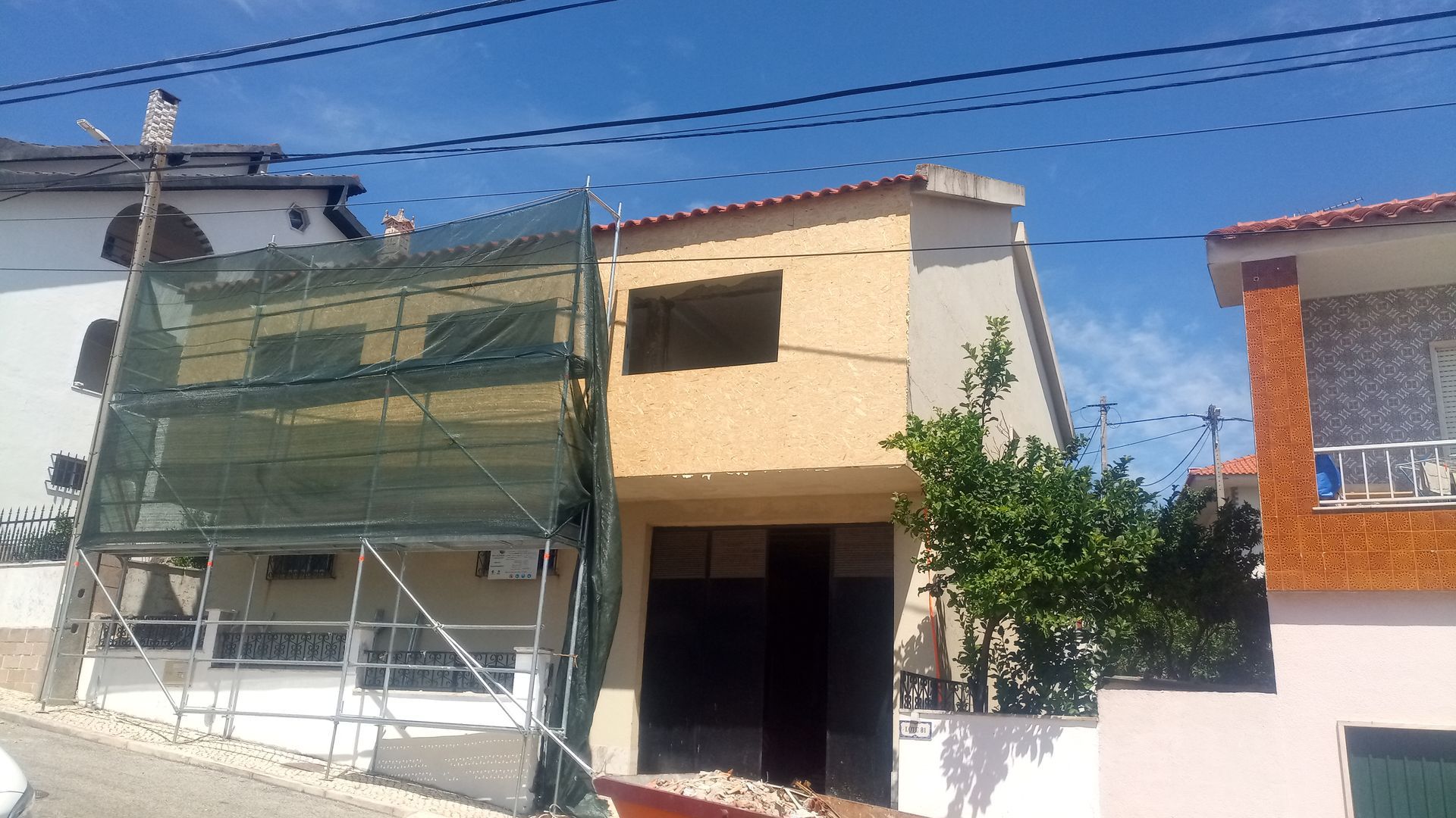 Prédio em construção, com andaimes e redes de proteção. Fachada em tons de bege e creme. Céu limpo.