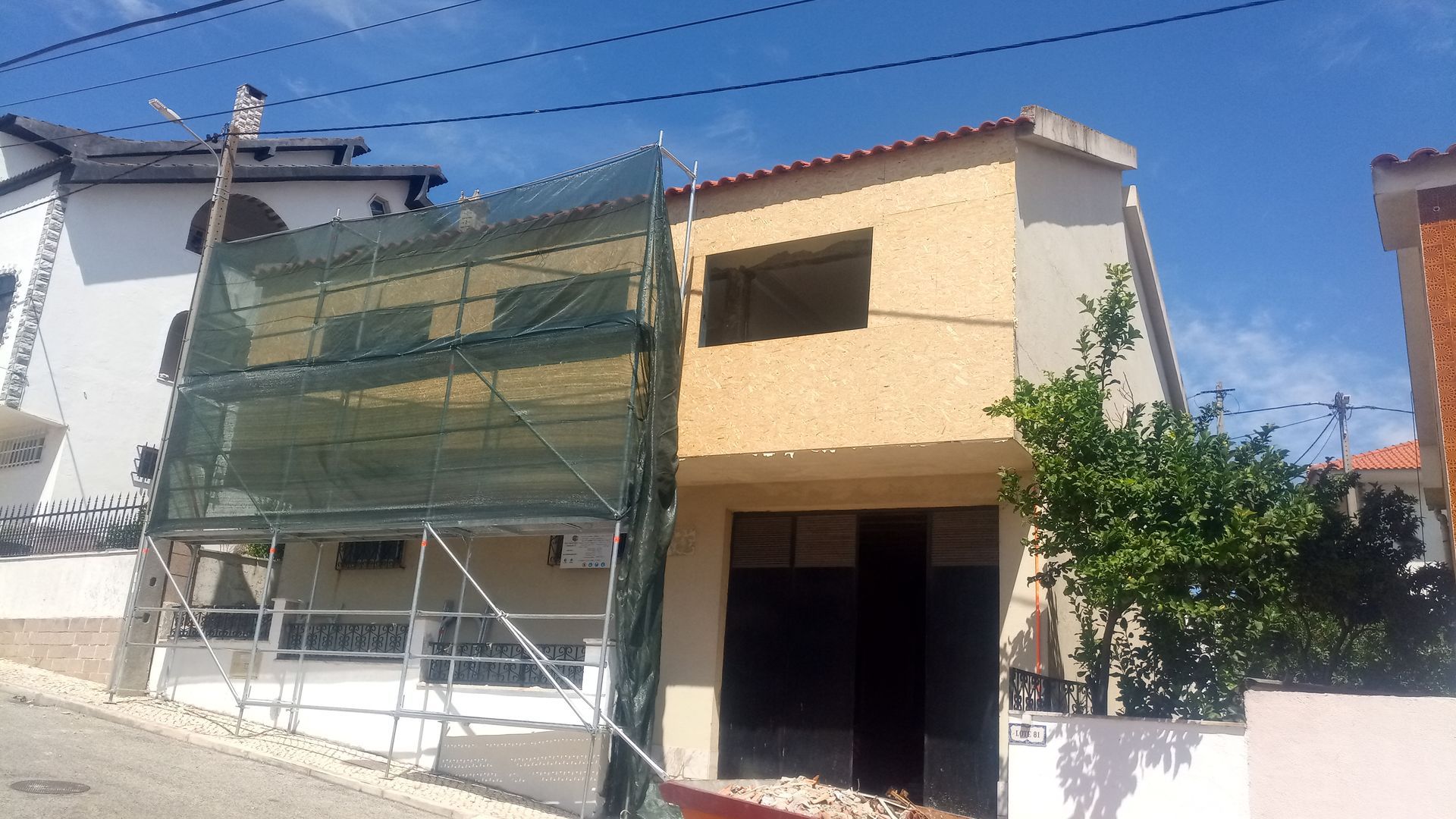 Prédio em construção com andaimes e redes de proteção, paredes bege, céu limpo.