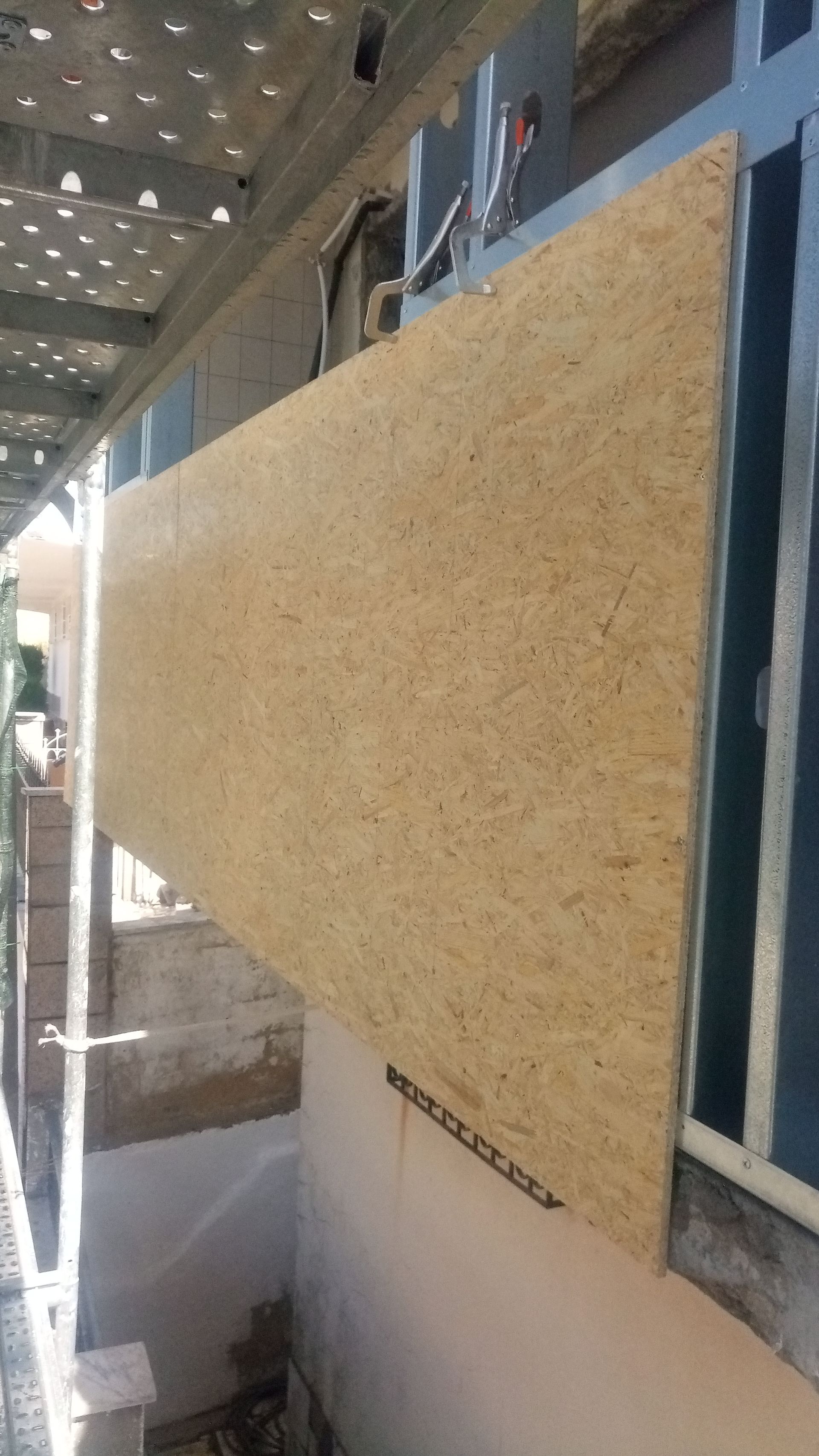 Placa OSB instalada na fachada de um edifício ao lado de uma janela; canteiro de obras.