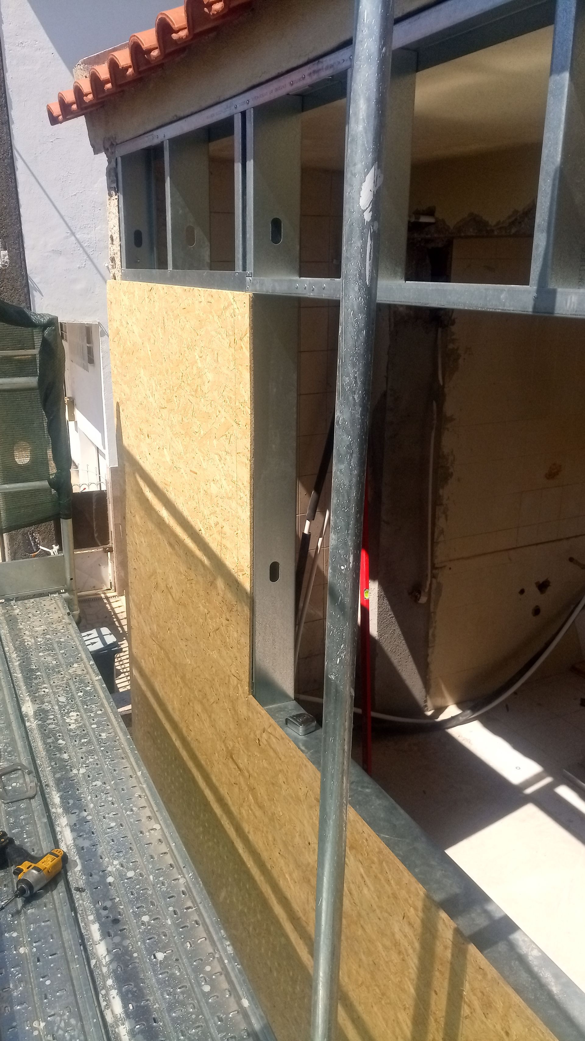 Canteiro de obras com andaimes. A fachada de um edifício mostra uma parede parcialmente concluída e a moldura de uma janela visível.