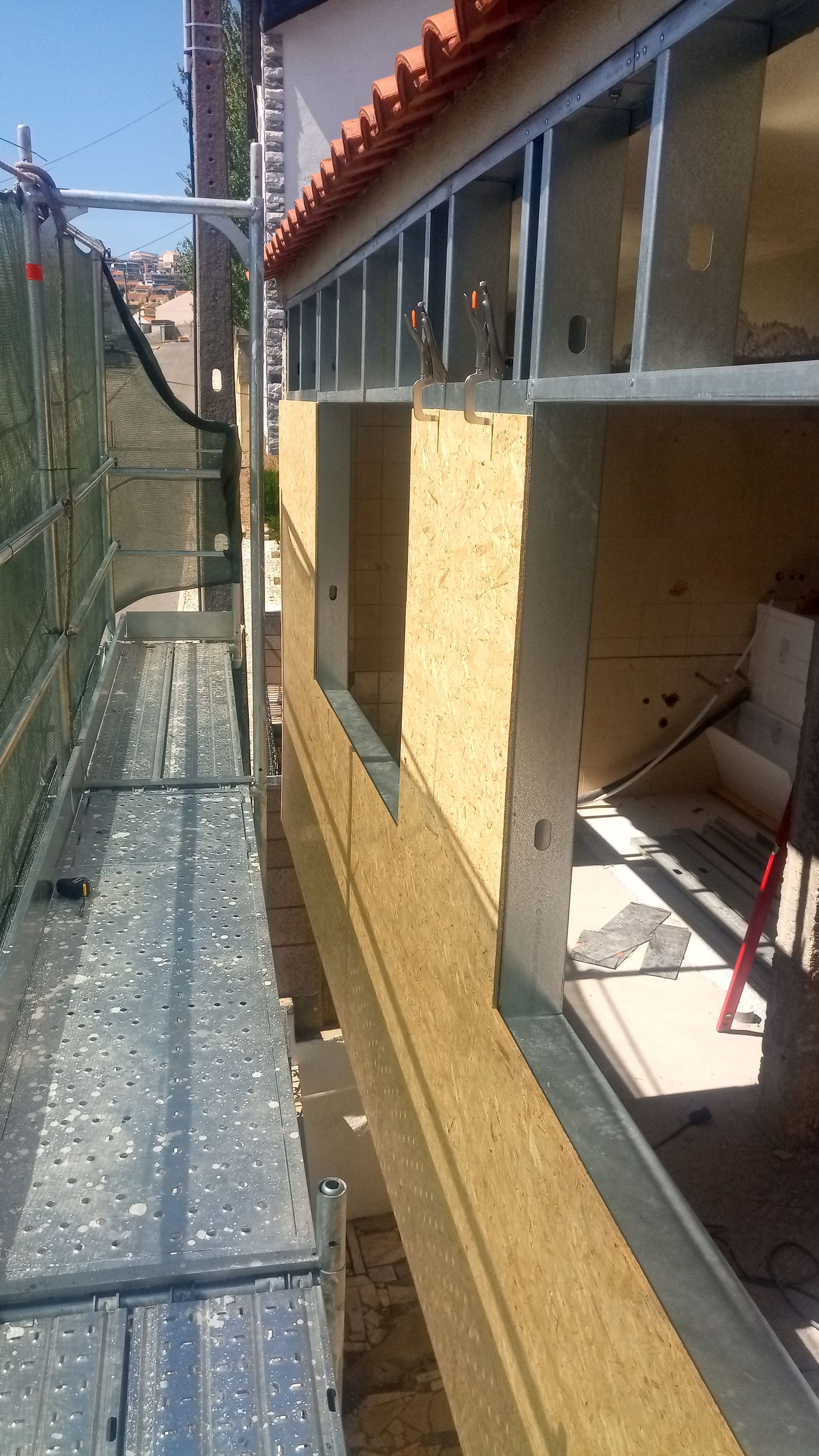 Canteiro de obras: andaimes ao lado de um prédio com janelas, parcialmente cobertos com isolamento.