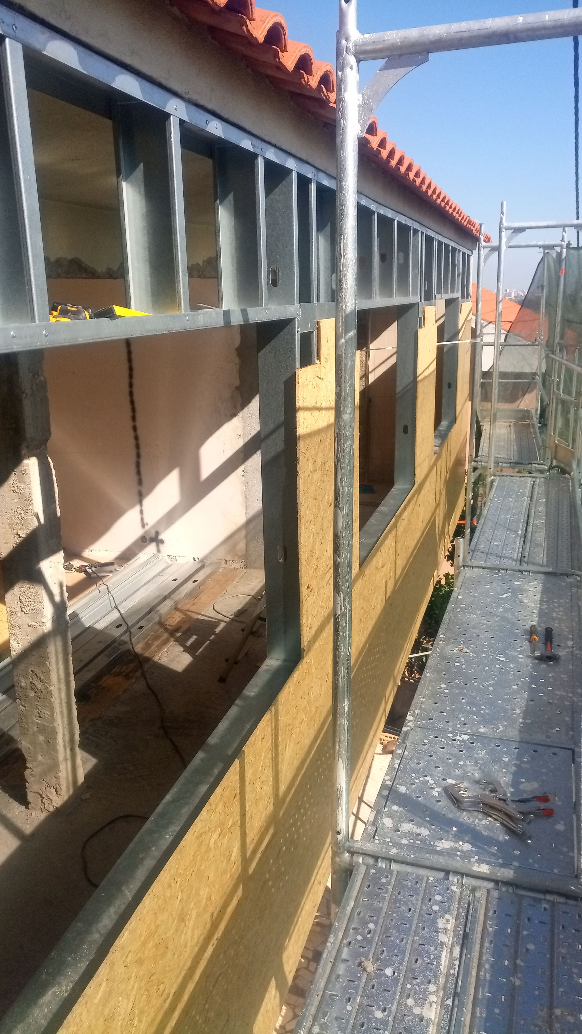 Construção de paredes externas com andaimes, estrutura metálica, isolamento e aberturas para janelas.