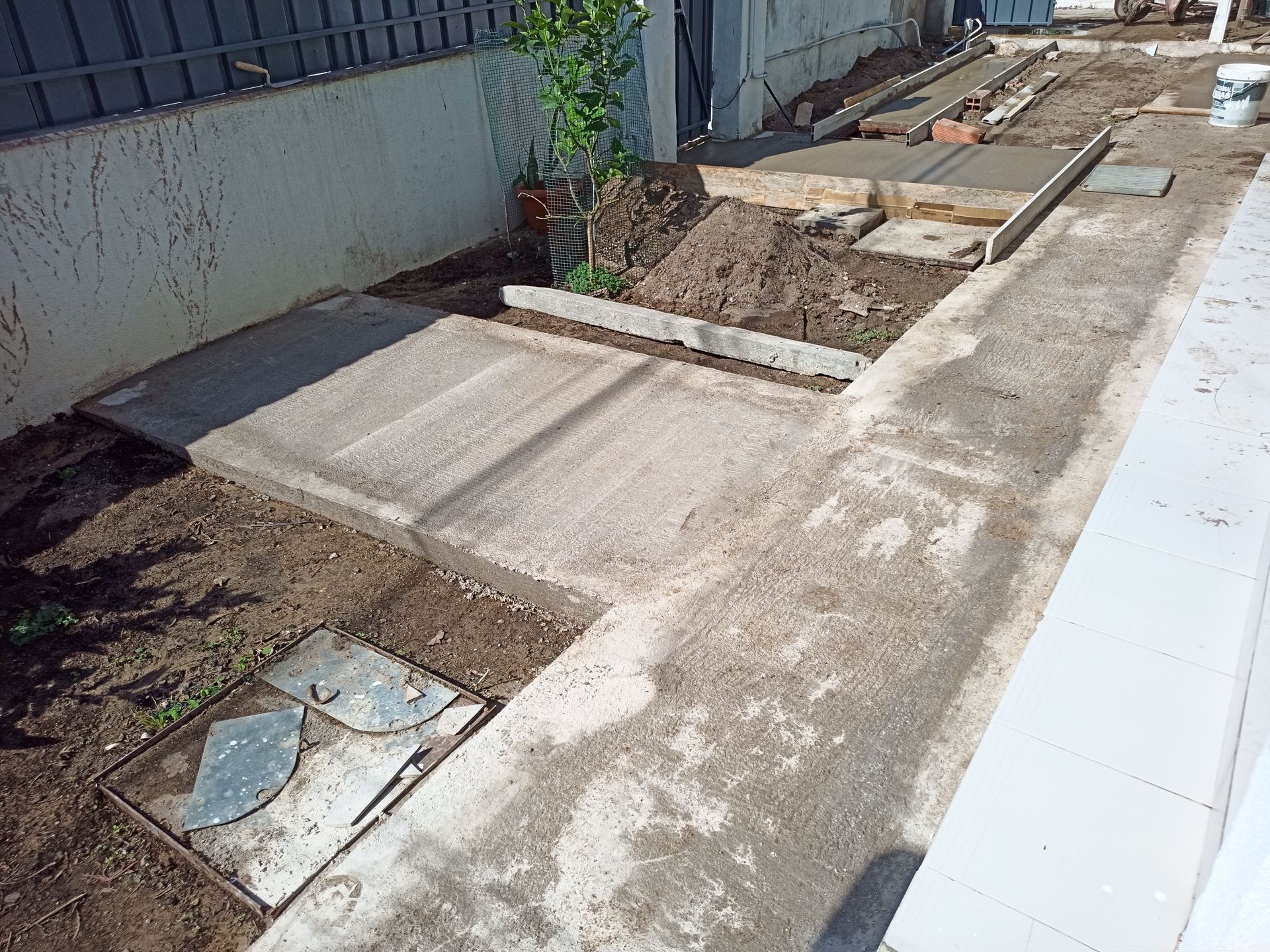 Passarela de concreto com trechos inacabados e solo exposto, ao lado de um prédio.