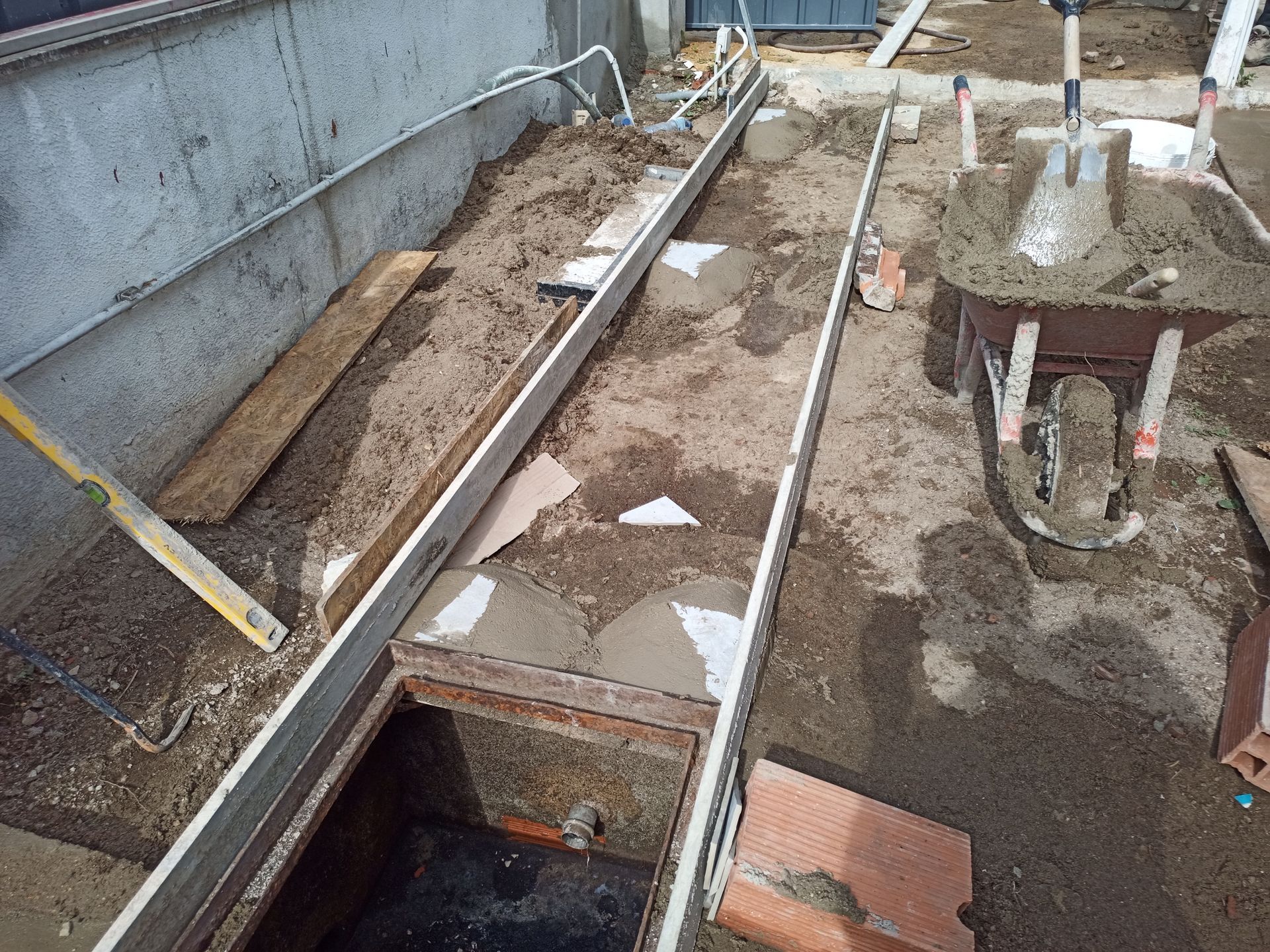 Canteiro de obras: canal de concreto em construção, com tampa de bueiro visível. Ferramentas e materiais estão próximos.
