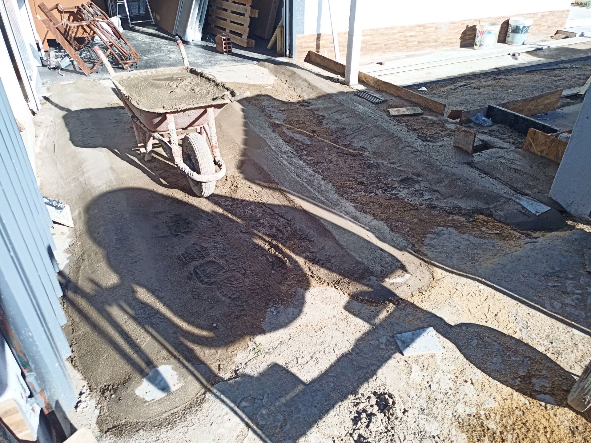 Carrinho de mão em um canteiro de obras de concreto, projetando uma longa sombra em um dia ensolarado.