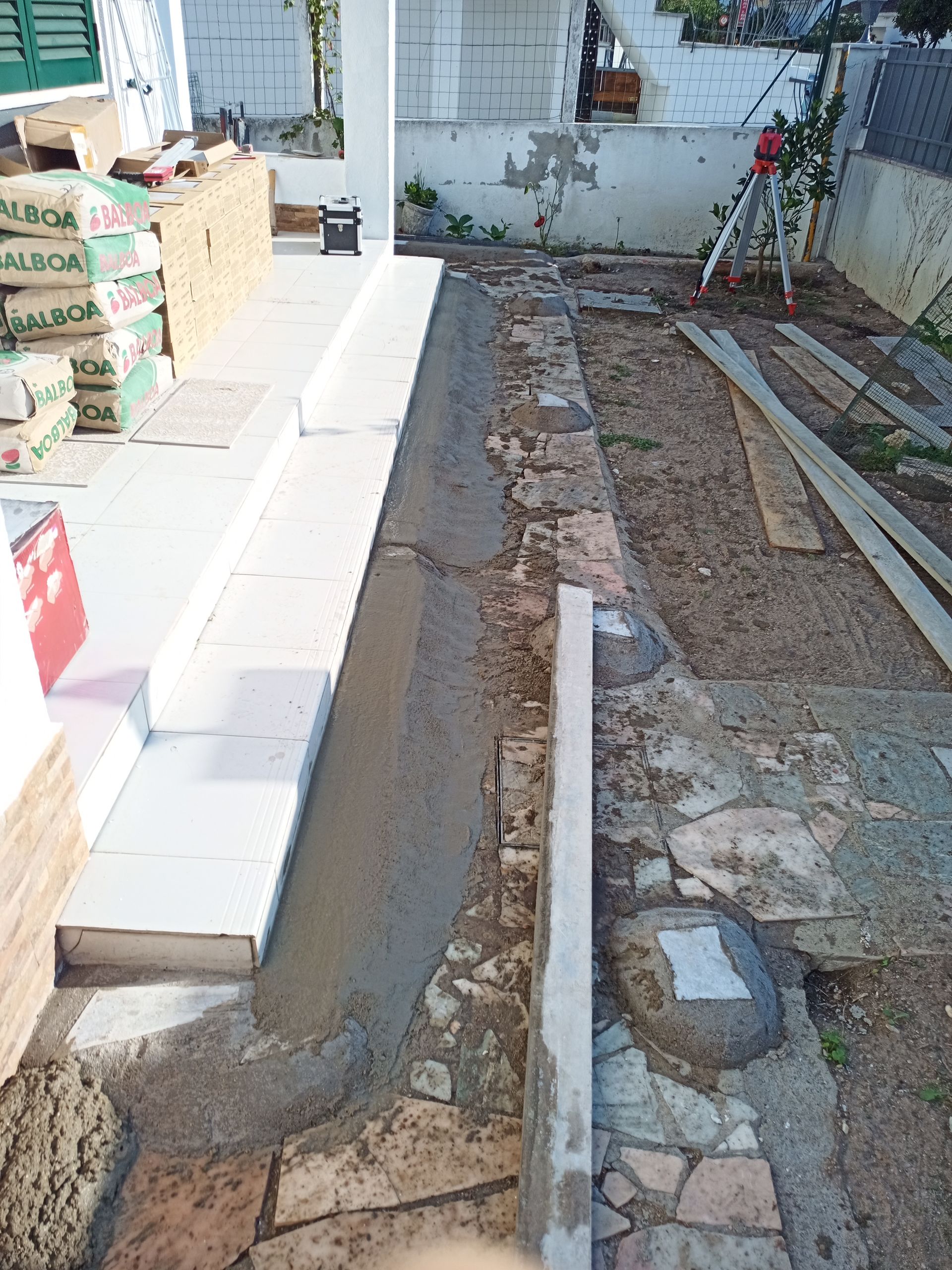 Canteiro de obras com concreto recém-assentado, caminho de pedra e materiais de construção.