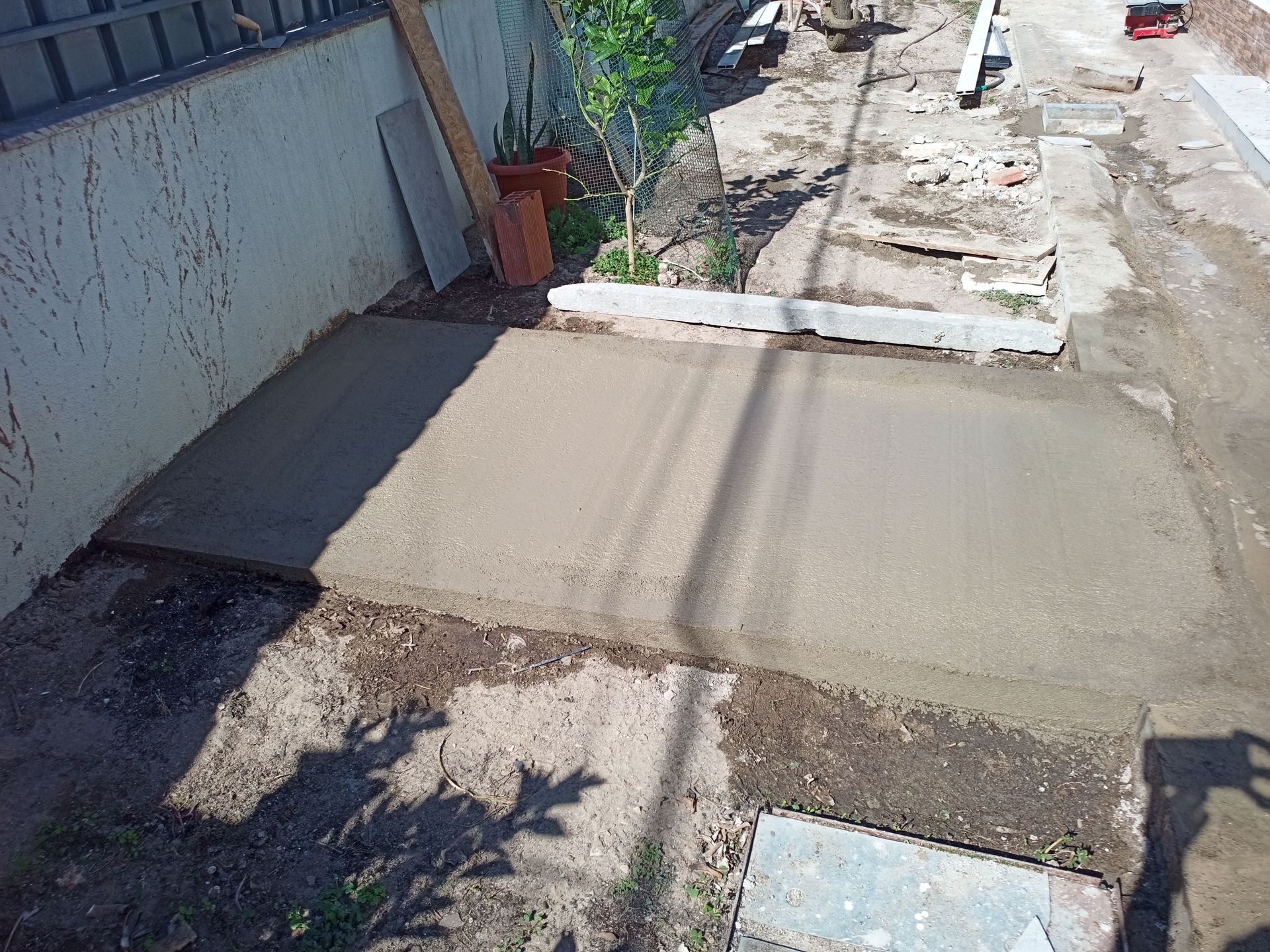 Laje de concreto recém-construída; ambiente externo com algumas ferramentas, plantas e parte de uma cerca.