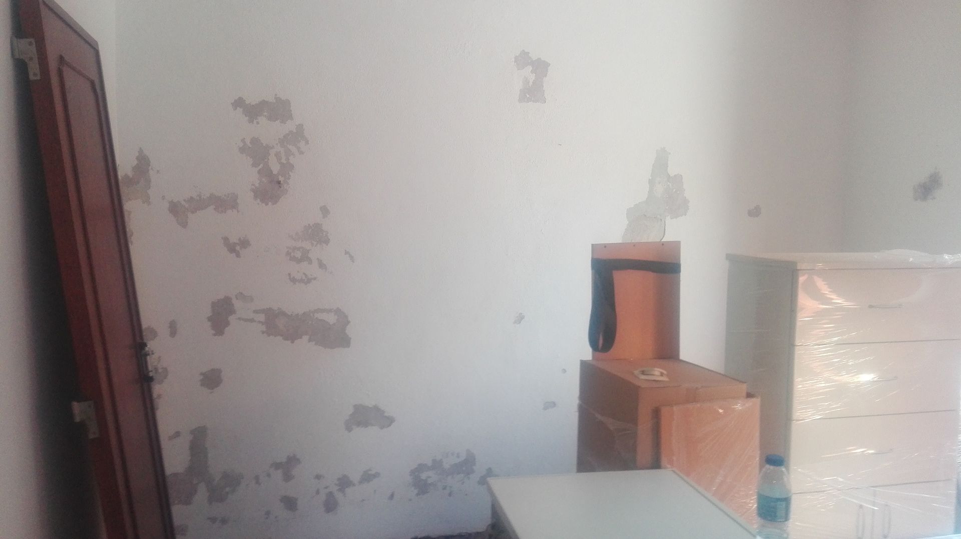 Parede com tinta descascando, uma porta de madeira e duas caixas de madeira em tons de branco e laranja.