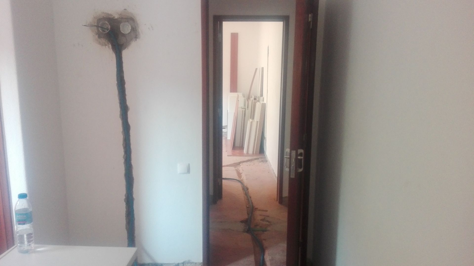 Corredor em construção com fiação exposta e porta aberta para outro cômodo.