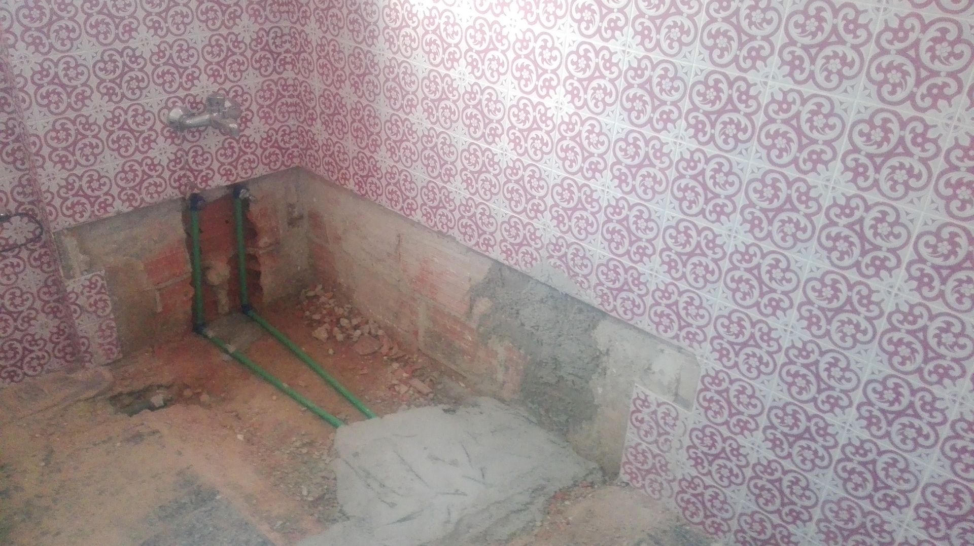 Reforma de banheiro em andamento com papel de parede estampado, canos aparentes e área da banheira inacabada.