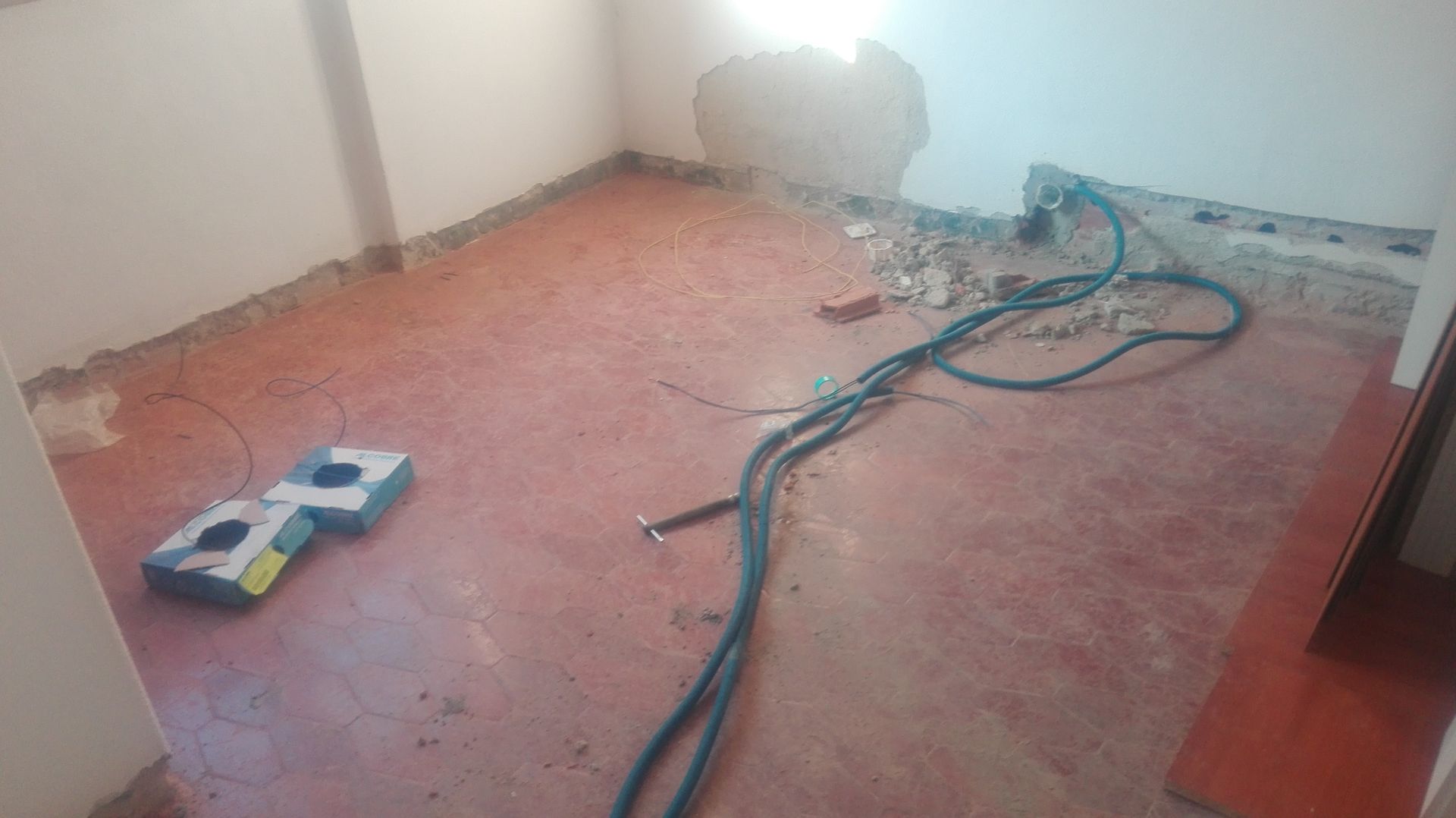 Sala em construção com piso vermelho, parede exposta, cabos elétricos e equipamentos.