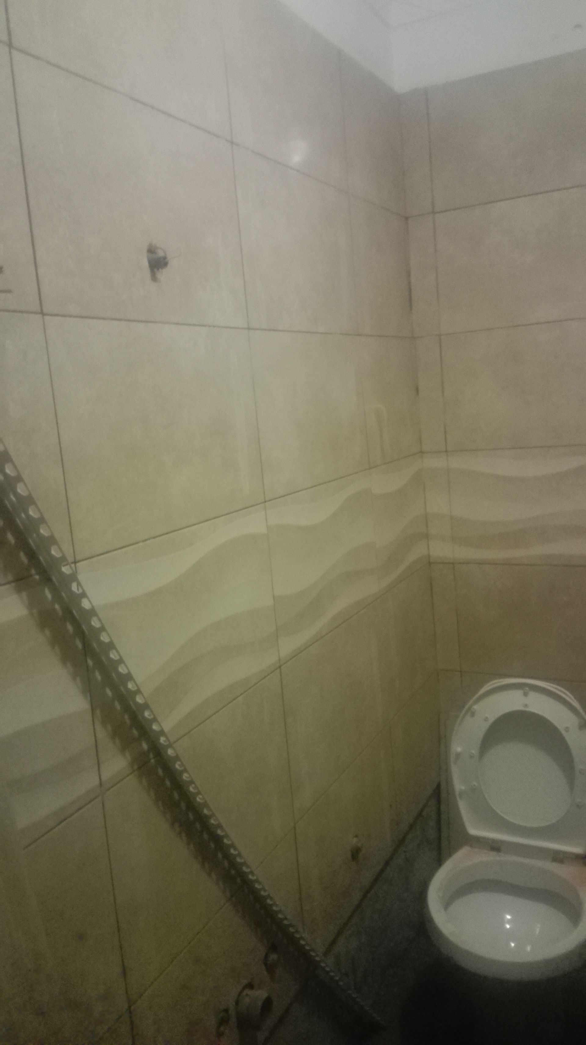 Banheiro com paredes revestidas de azulejos, vaso sanitário e objeto de metal encostado na parede.