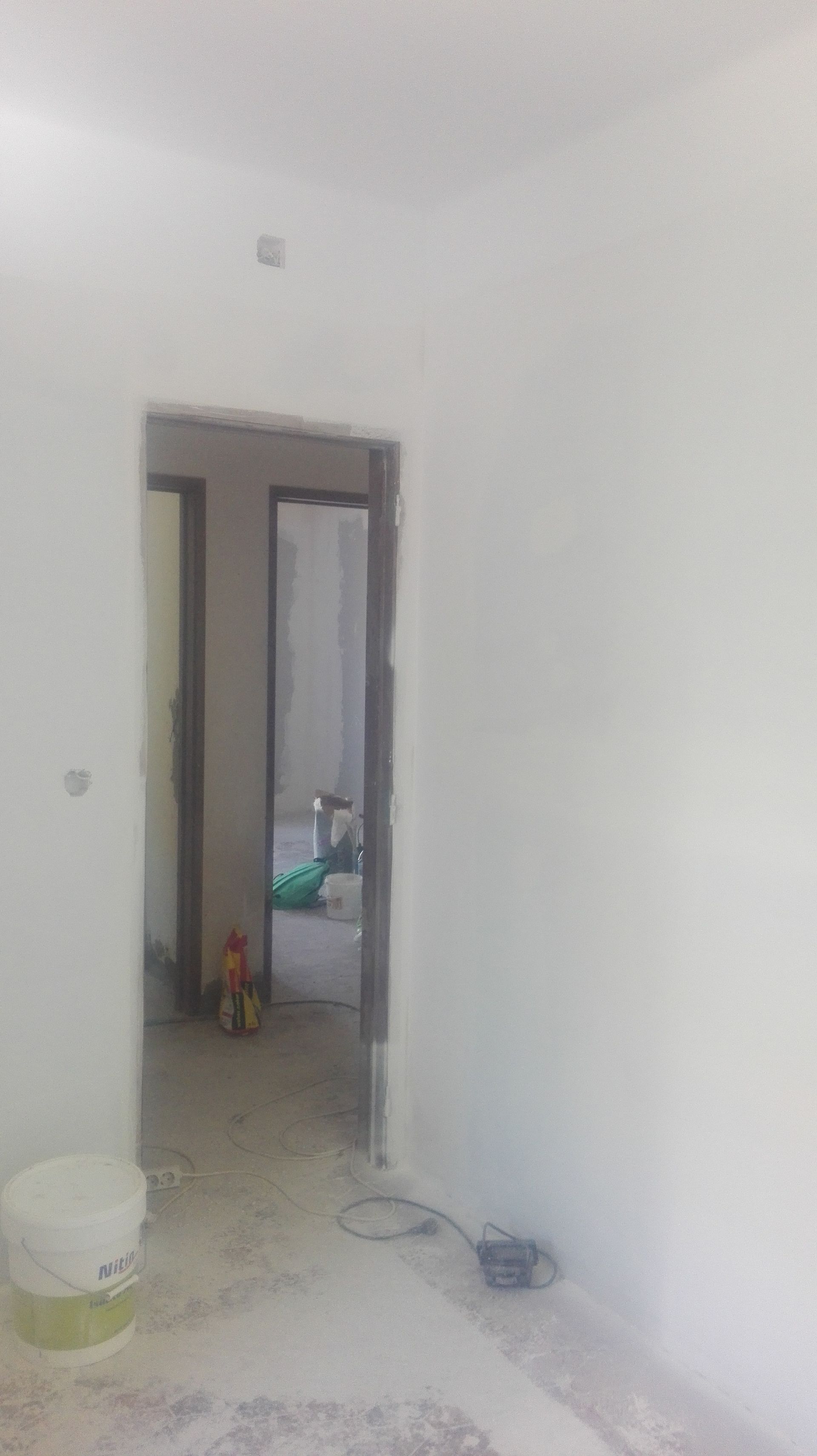 Interior de um quarto com uma porta, paredes brancas e um balde no chão.