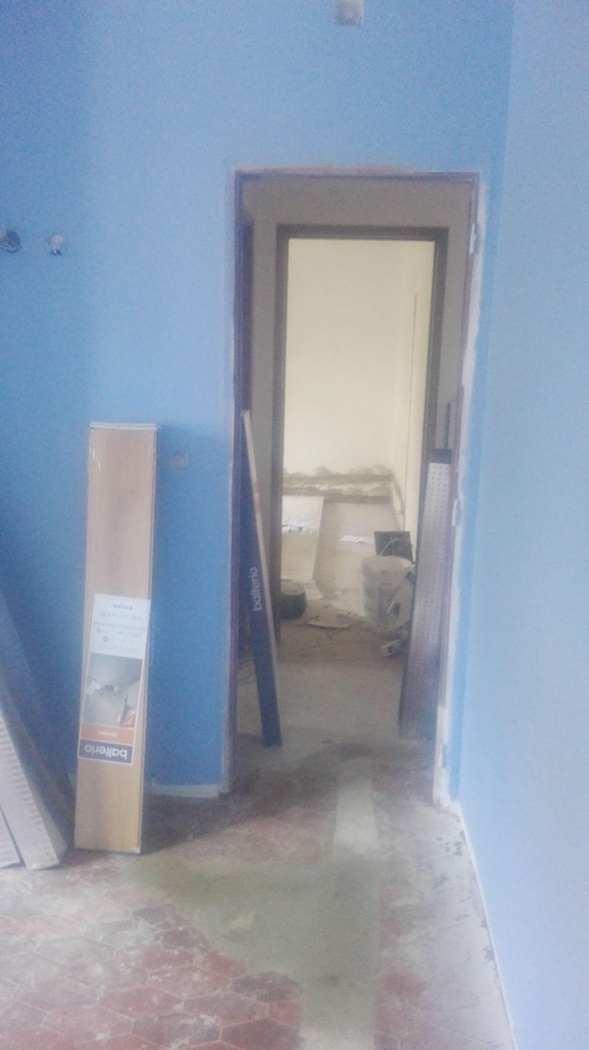 Paredes azuis com uma porta que dá para outro cômodo; materiais de construção encostados por perto.