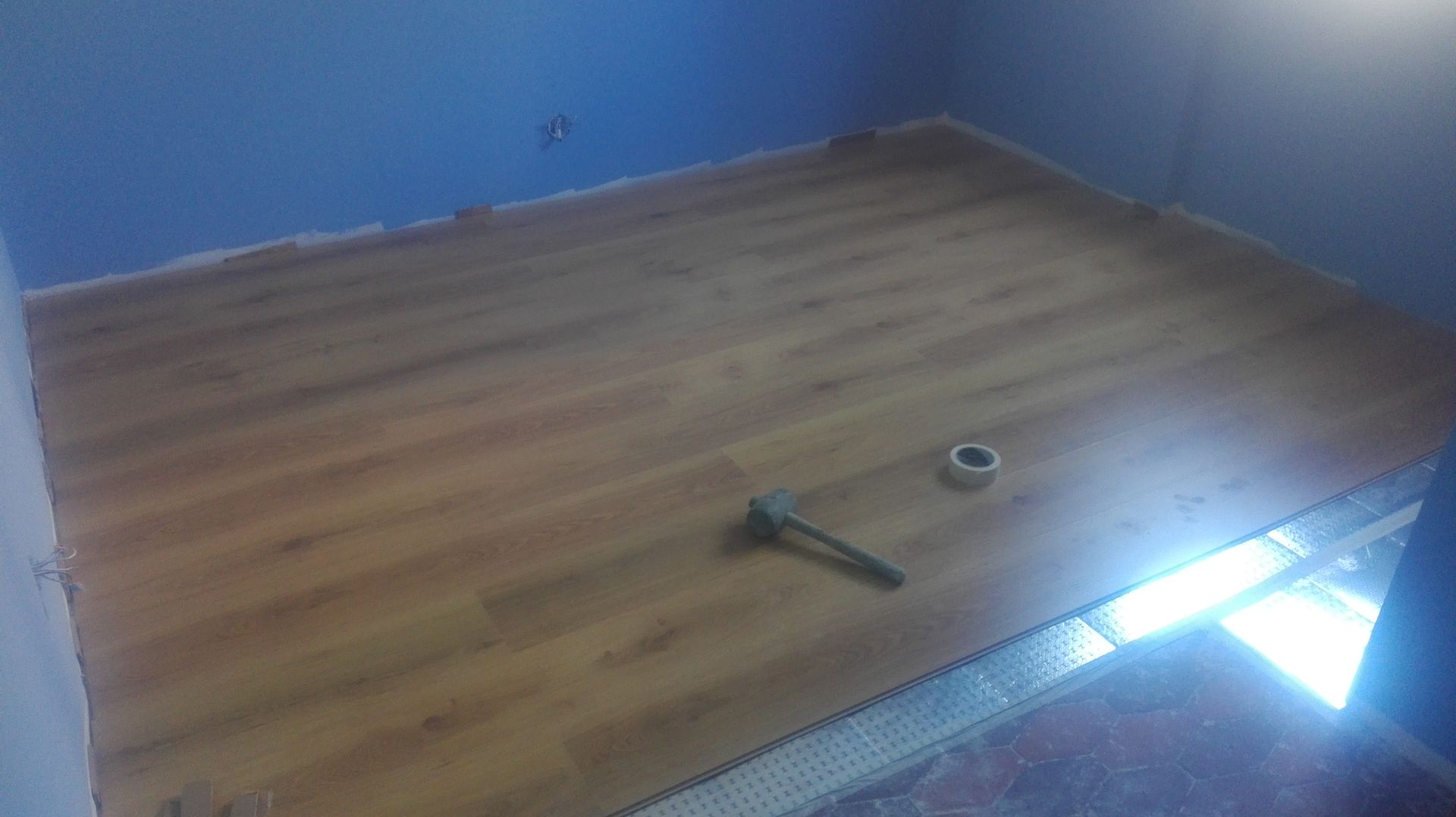 Instalação de piso de madeira em um cômodo com paredes azuis, com ferramentas e materiais presentes.