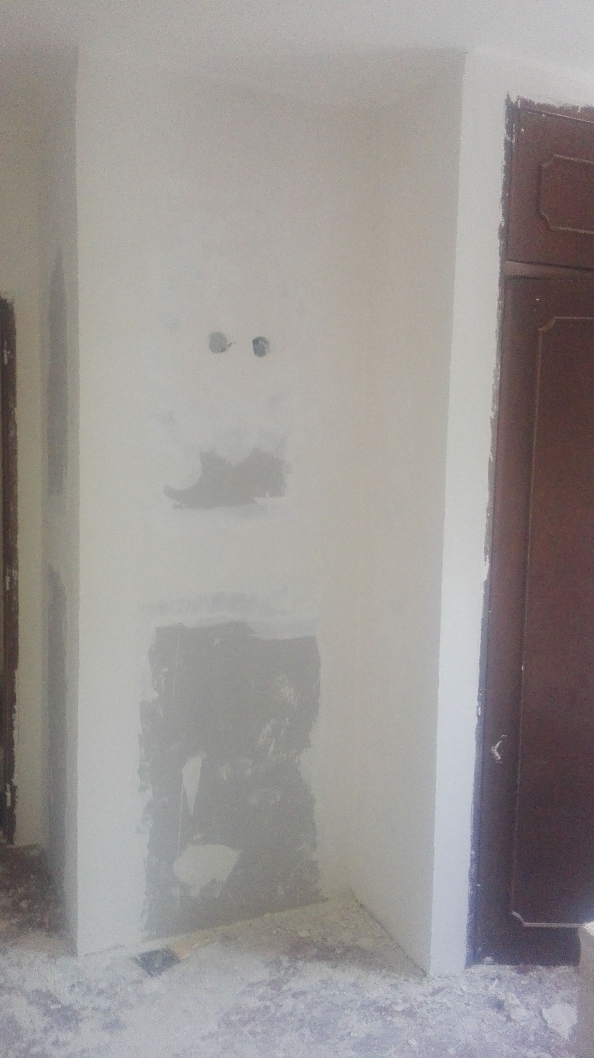 Parede com tomadas elétricas e reboco inacabado ao redor de uma porta.