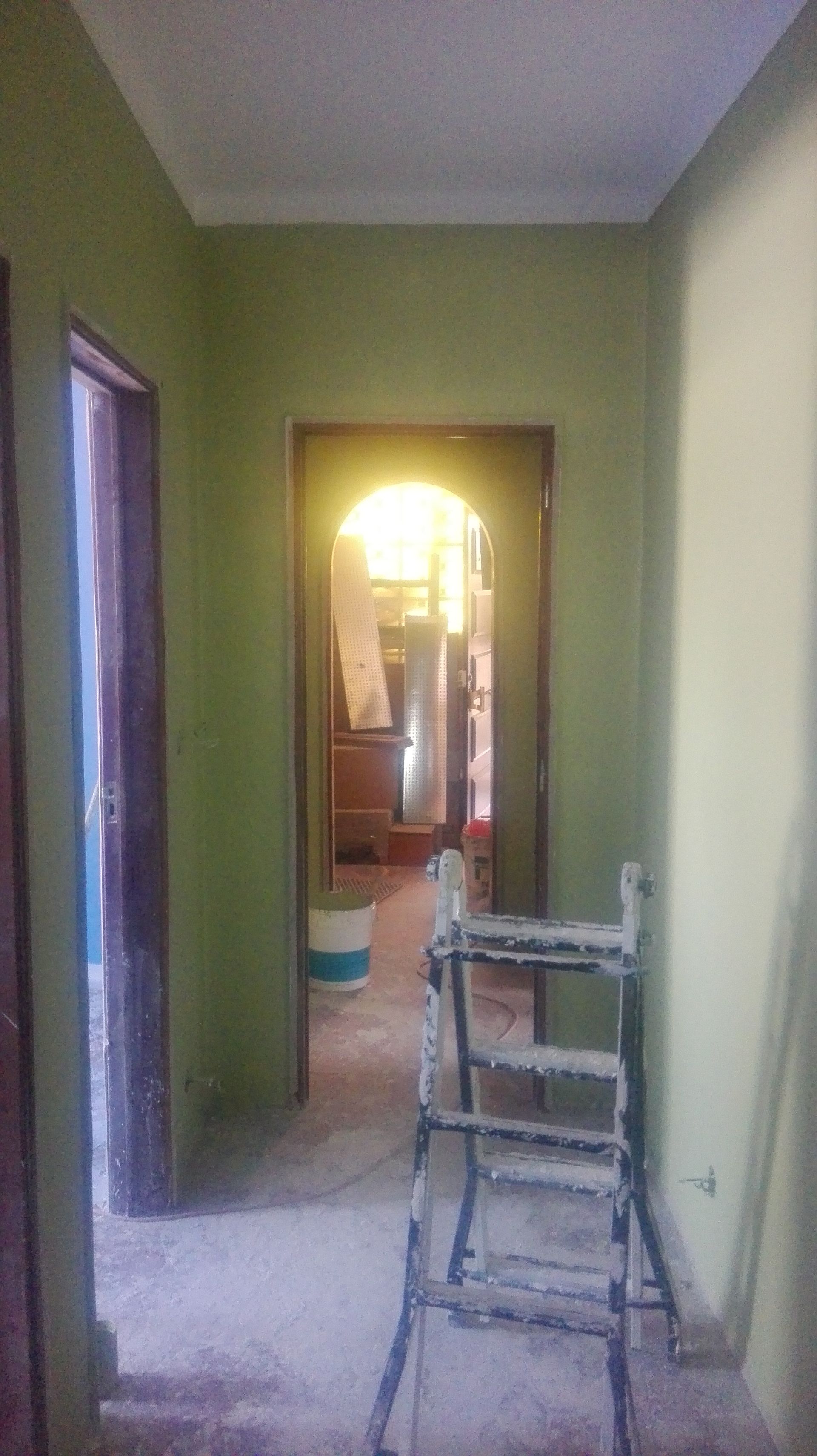 Corredor estreito com paredes verdes, portas abertas e uma escada.