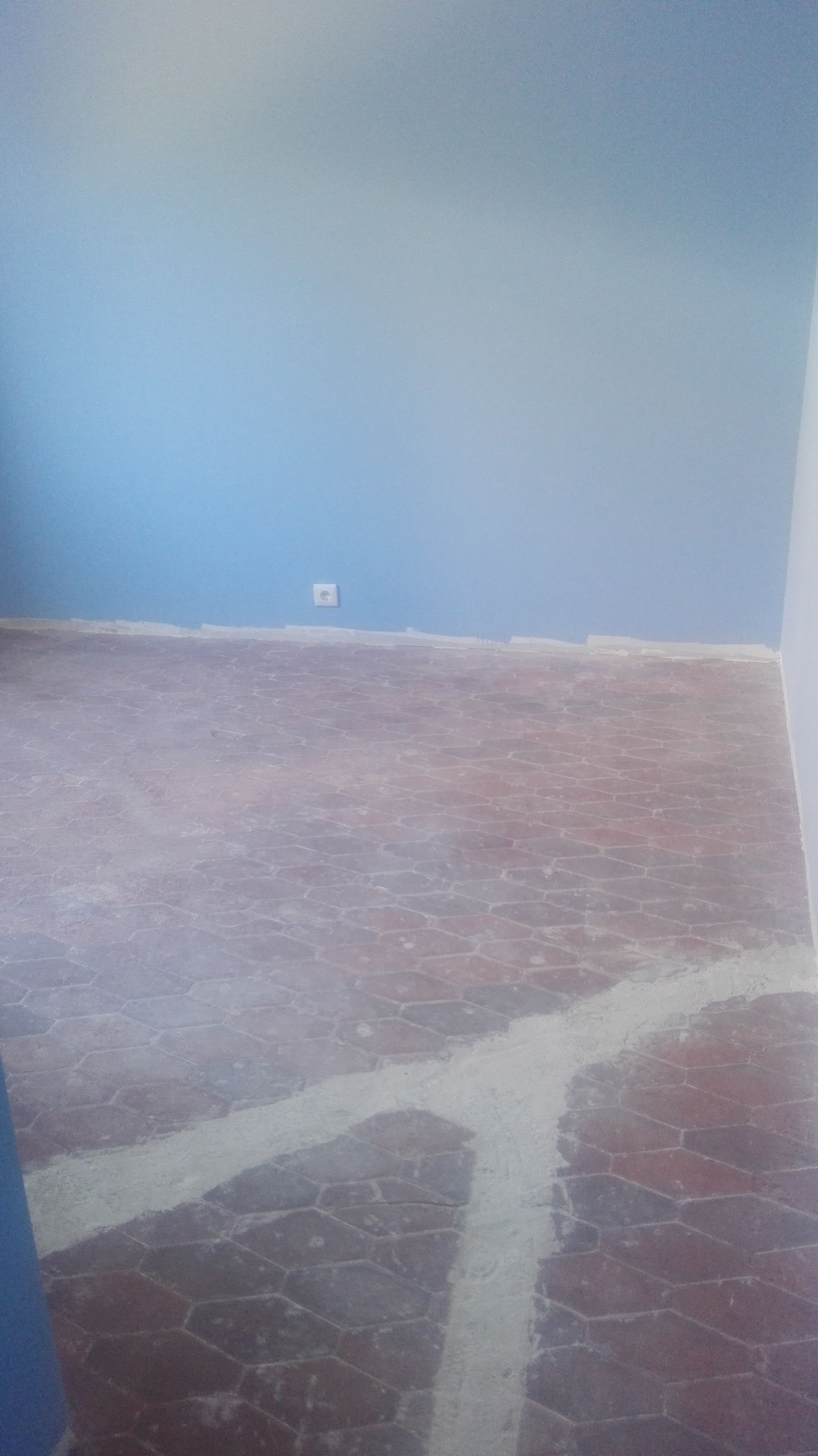 Parede azul e piso vermelho desgastado com marcas brancas.