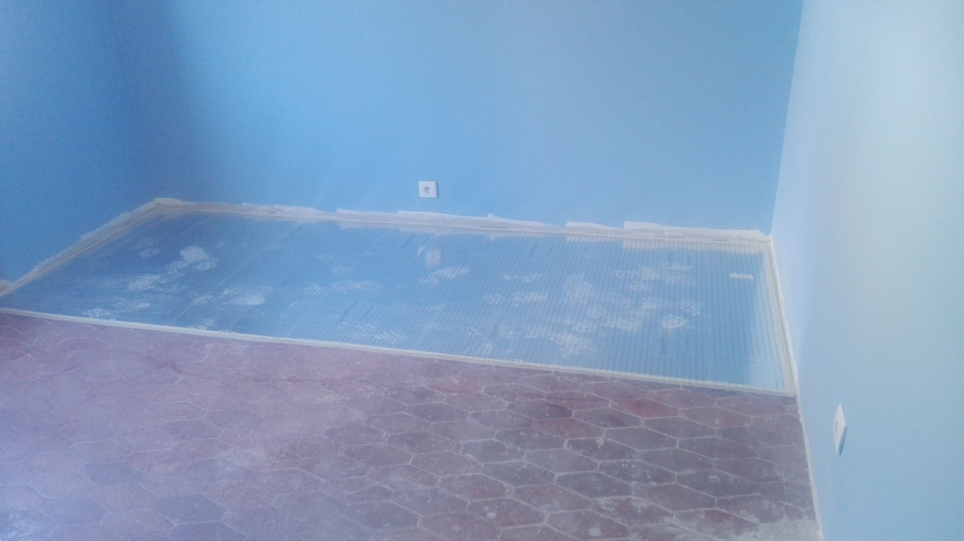 Quarto com paredes azuis, piso parcialmente acabado e uma tomada elétrica.