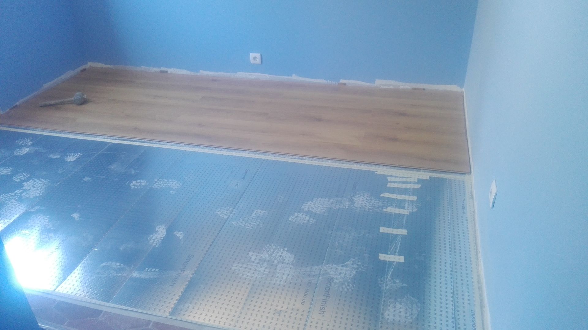 Quarto com paredes azuis, piso de madeira inacabado e contrapiso visível.