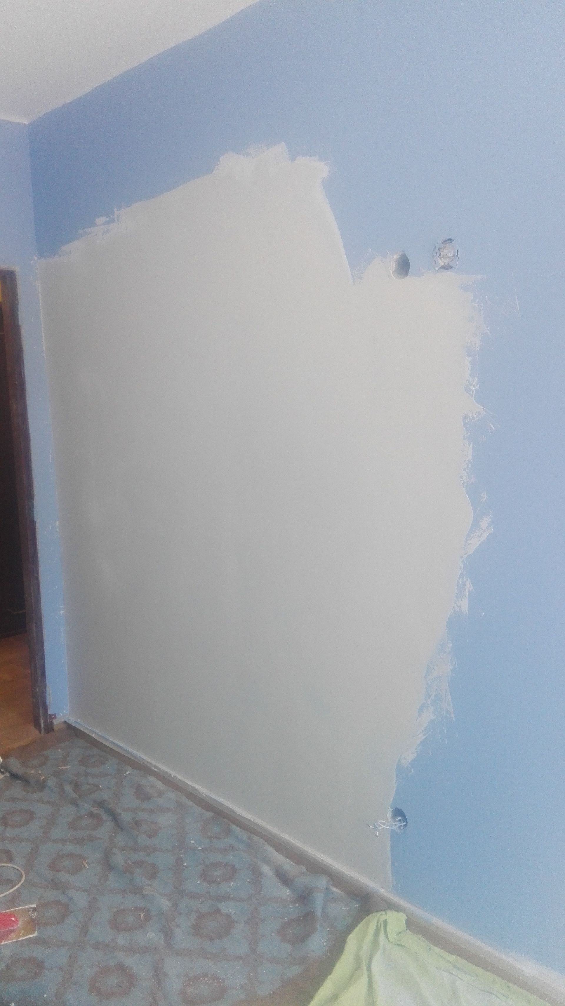 Parede parcialmente pintada de branco sobre parede azul, interior do quarto.