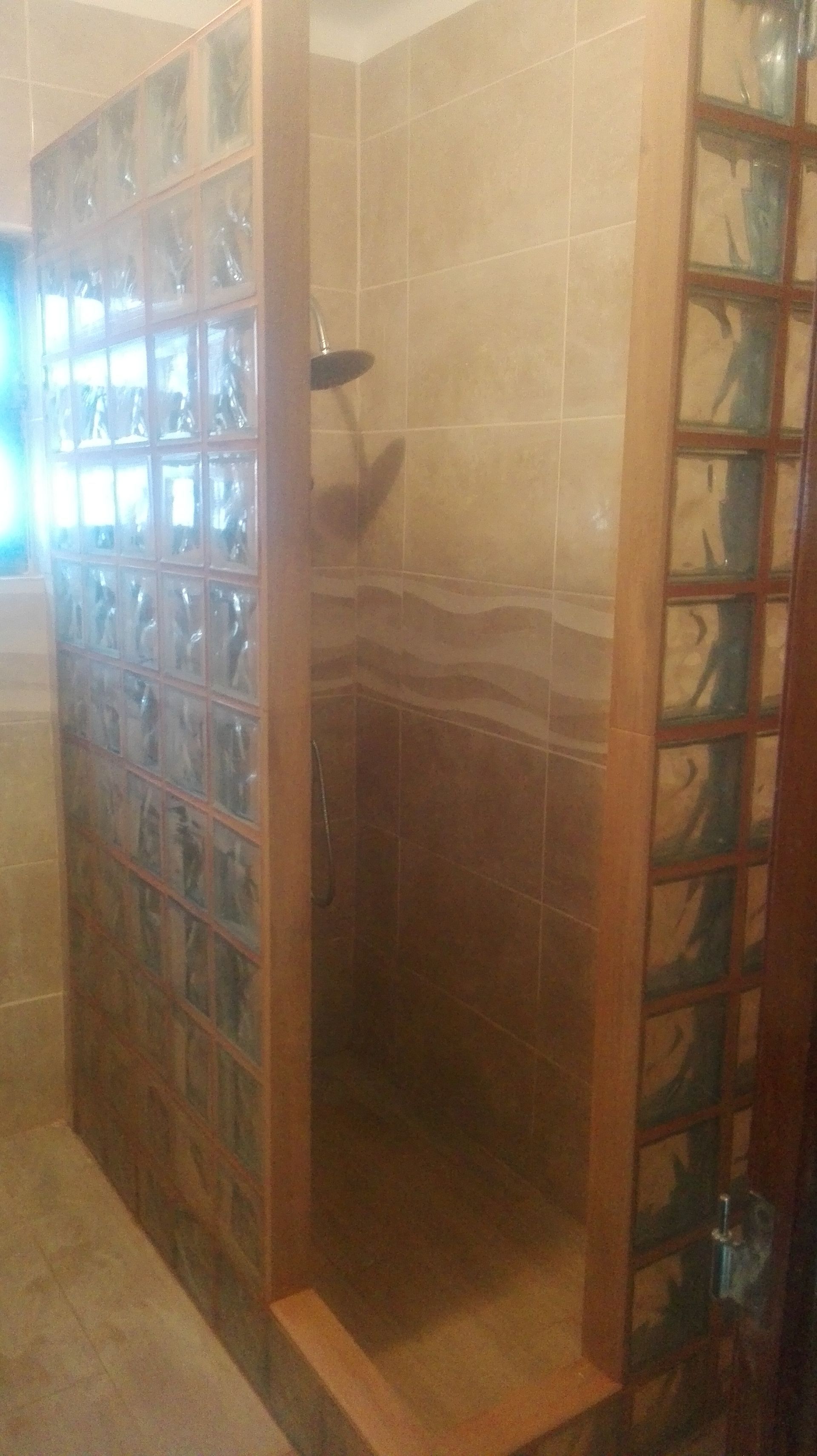 Cabine de duche com paredes de blocos de vidro, azulejo bege e estrutura de madeira.