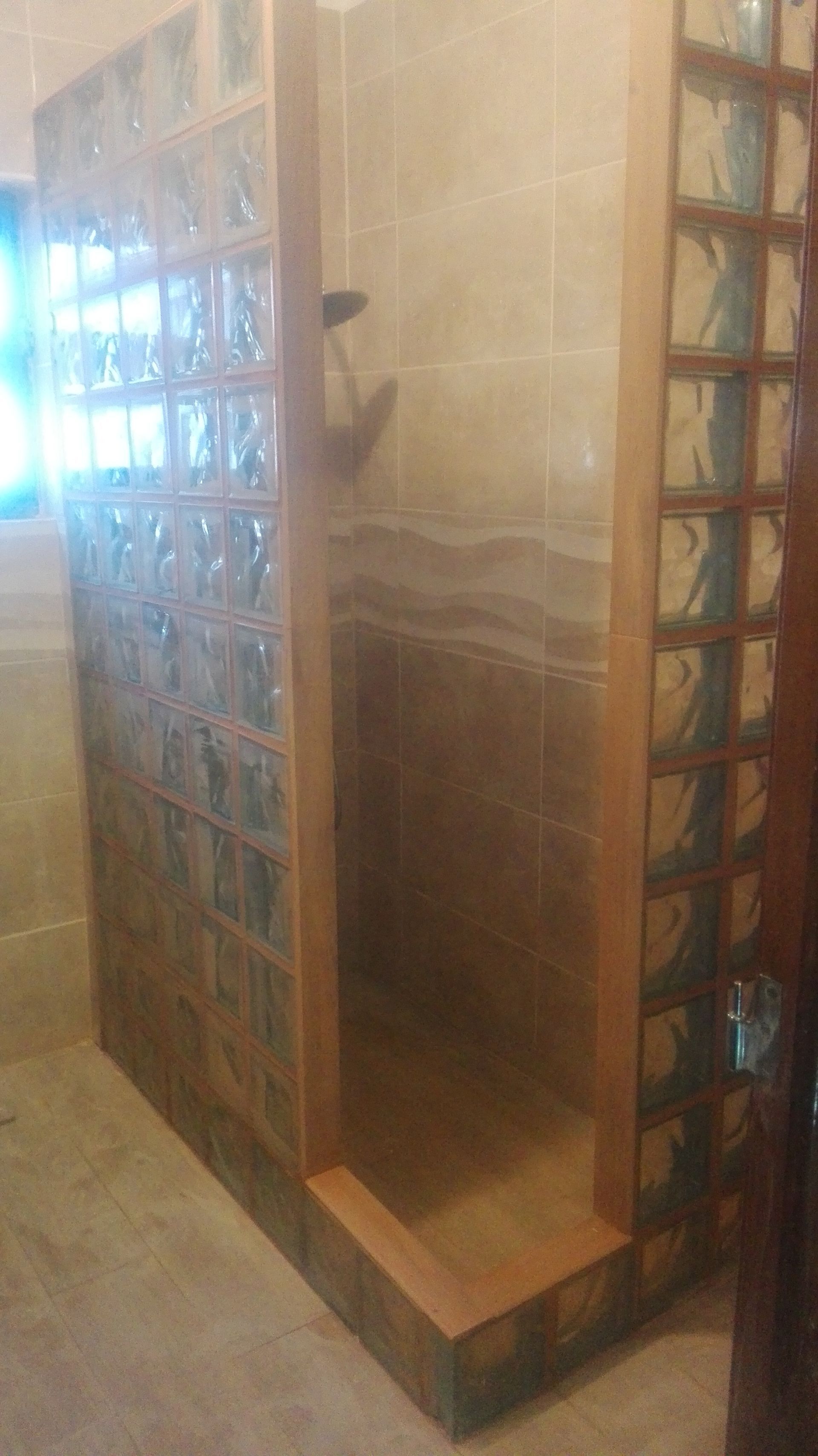 Cabina de duche com paredes de blocos de vidro e estrutura de madeira. Azulejos interiores em tons de bege e castanho.