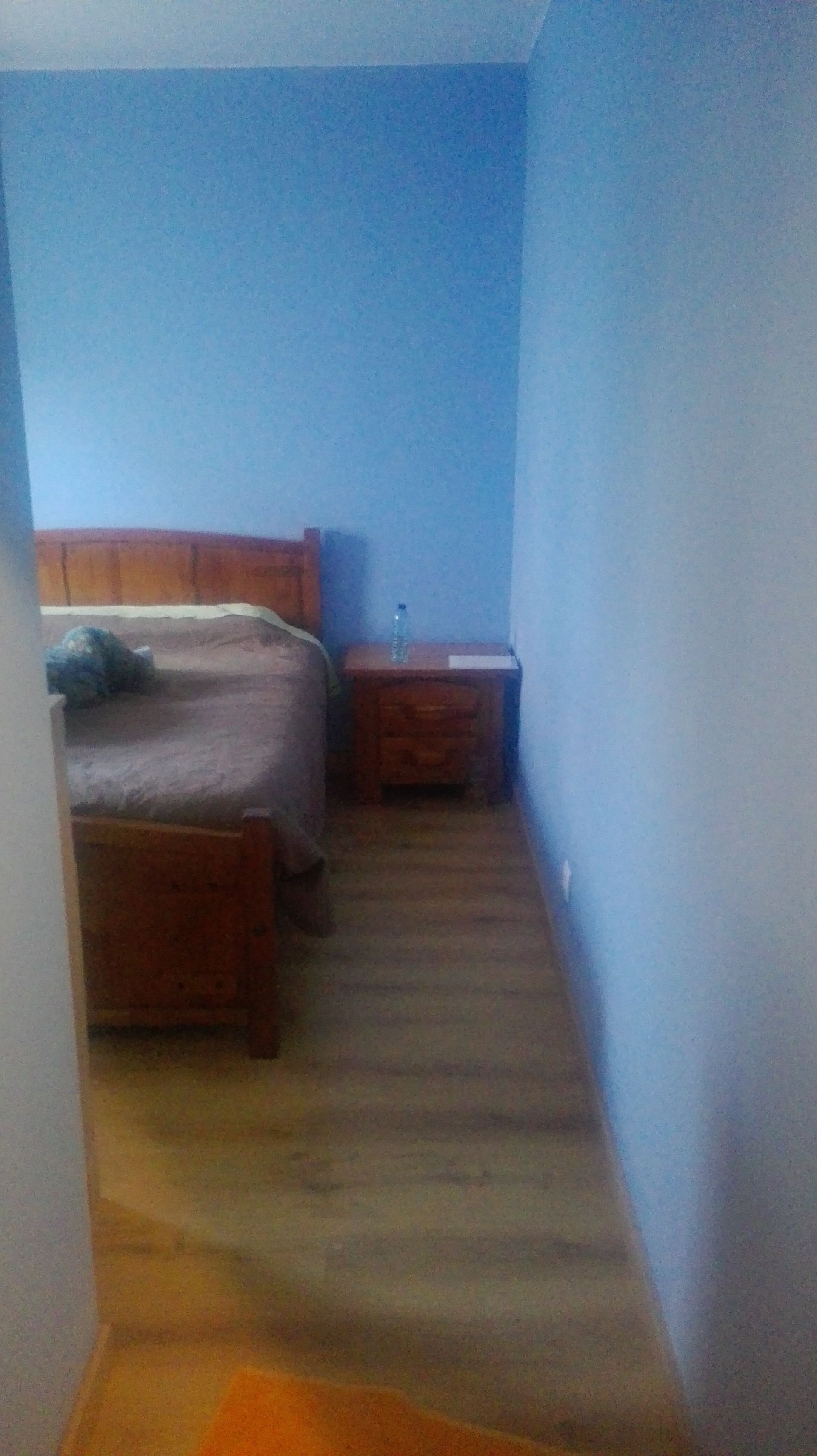 Quarto com cama de madeira, mesa de cabeceira, paredes azuis e piso de madeira clara.