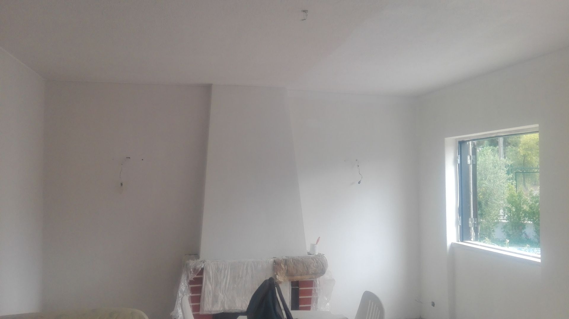 Sala com paredes brancas, lareira e janela; a área sob a lareira é revestida de tijolos.