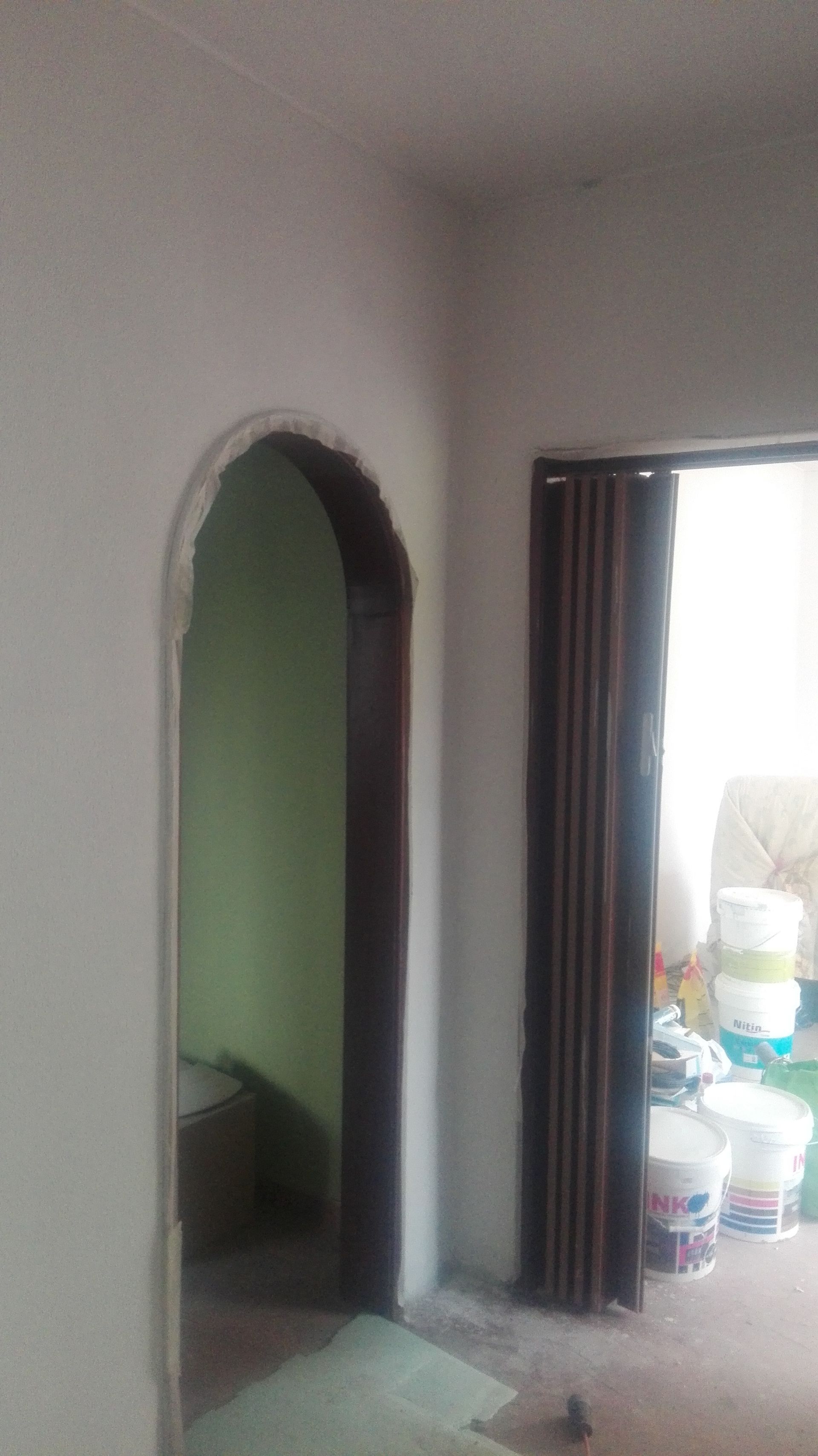 Vista interior da porta em arco e da porta sanfonada fechada. Paredes brancas, acabamento em madeira escura, parede verde-clara visível.