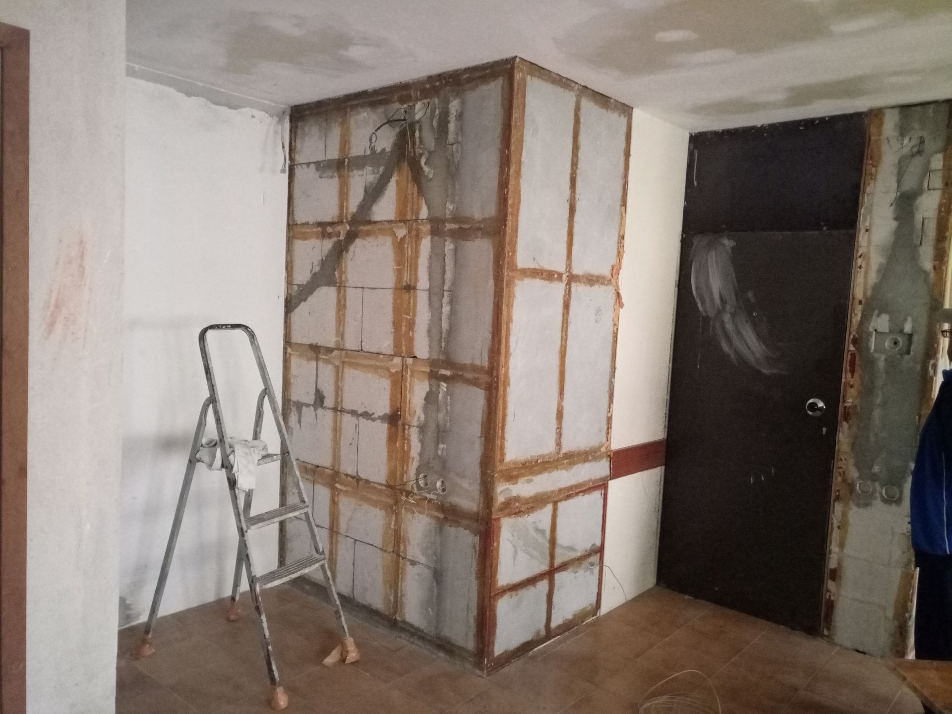 Quarto em construção com estrutura de madeira, escada e porta marrom escura.