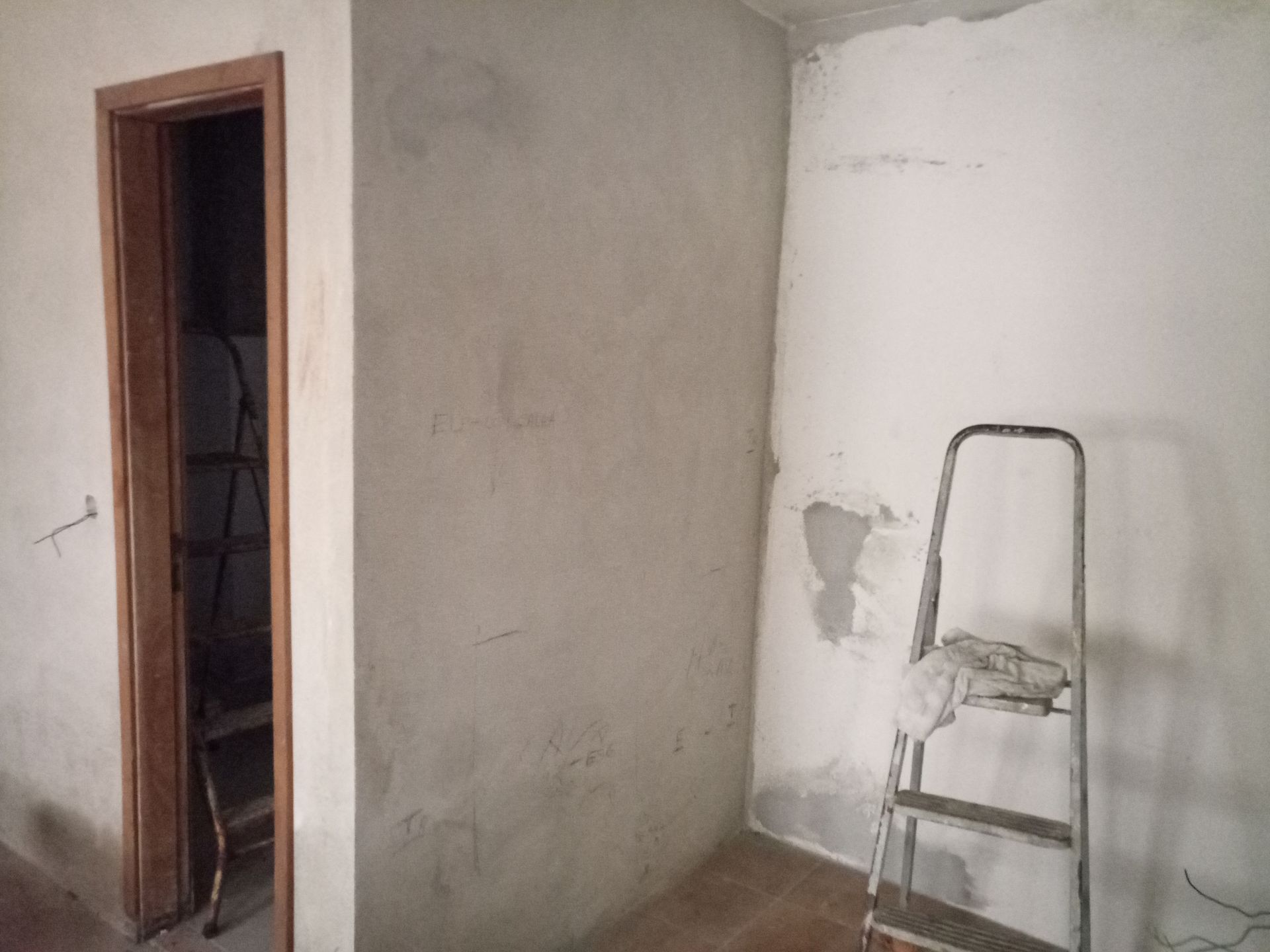 Interior de um cômodo com paredes rebocadas, porta e escada de mão.