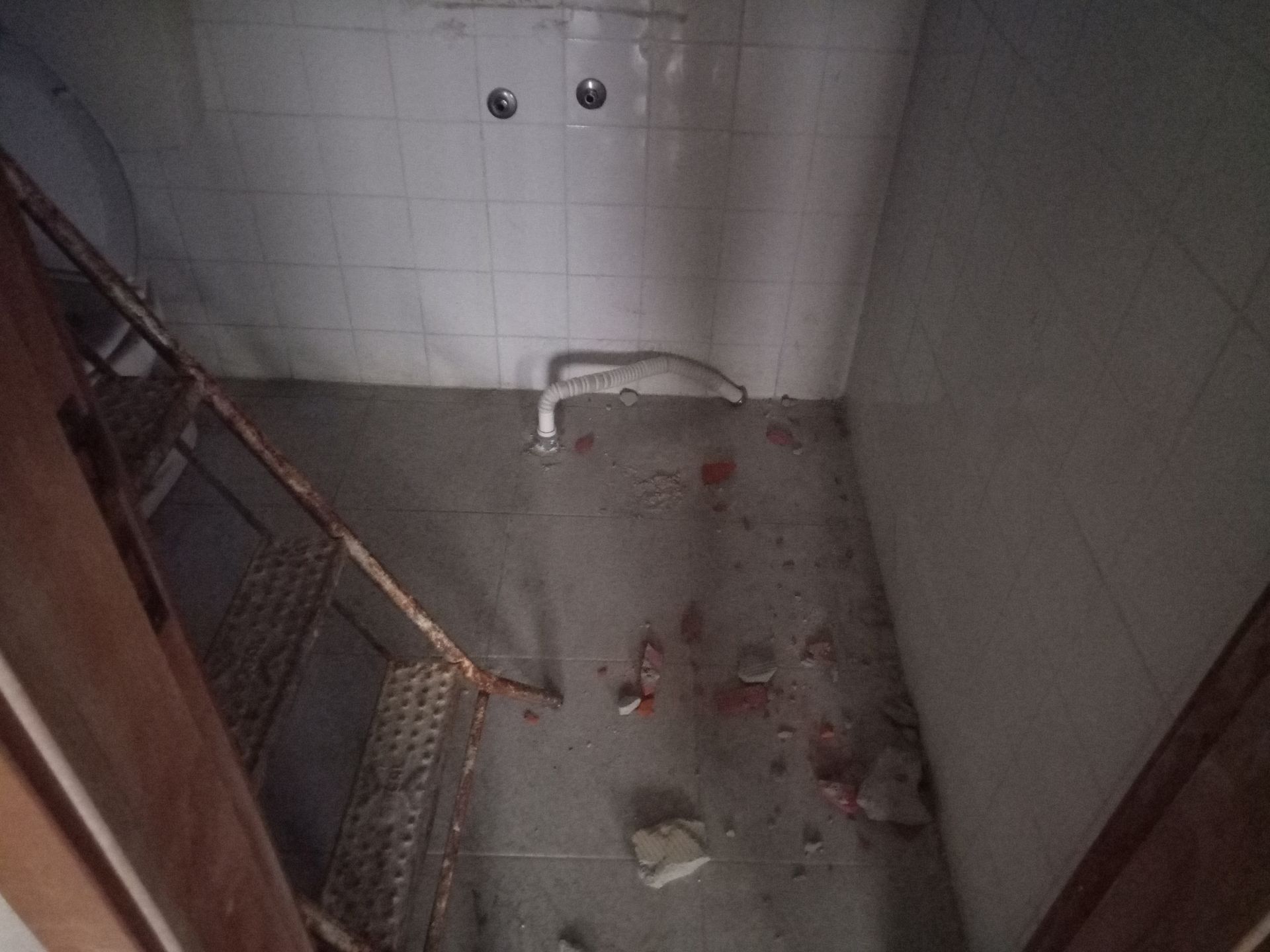 Um box de chuveiro com respingos de sangue no chão e barras enferrujadas.