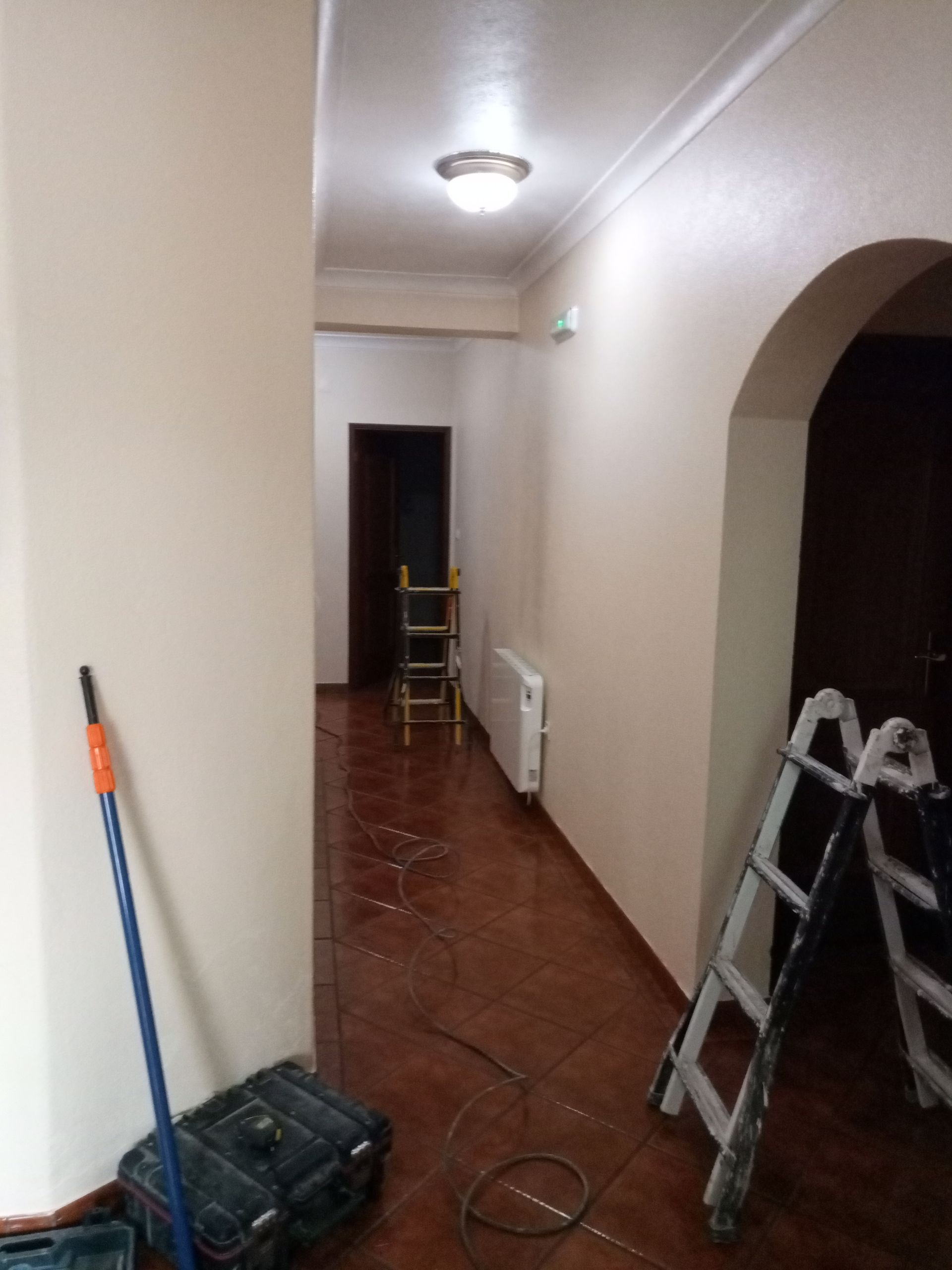 Corredor com paredes bege, piso de azulejo marrom e equipamentos de construção.