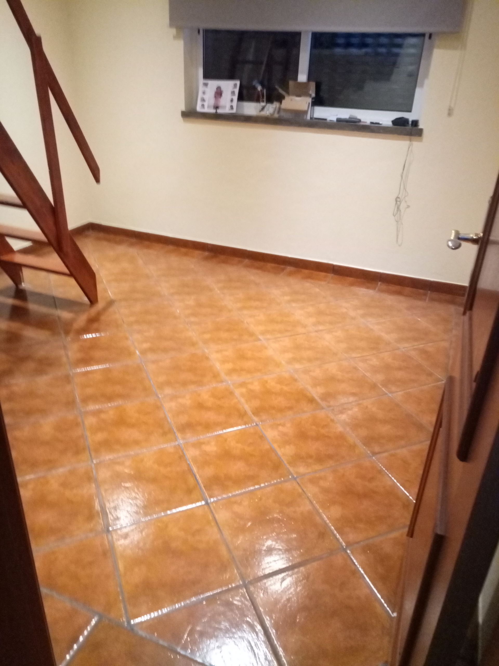 Quarto com piso de azulejo marrom, escadas, janela e paredes bege.