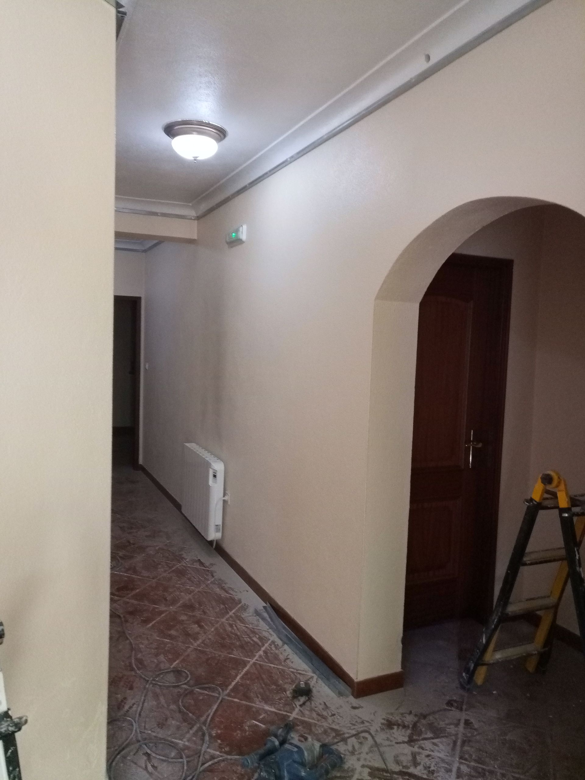 Corredor com paredes bege, porta em arco, porta marrom e radiador.