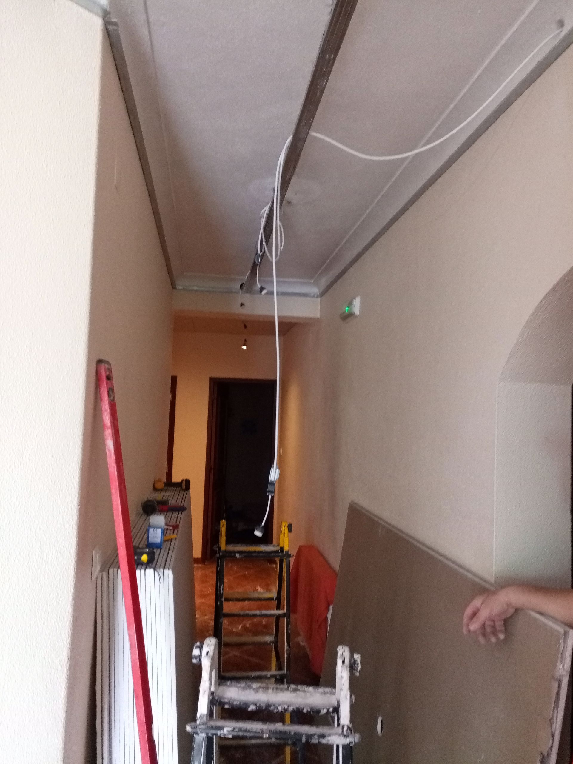Corredor estreito em reforma com fiação elétrica, ferramentas e drywall.