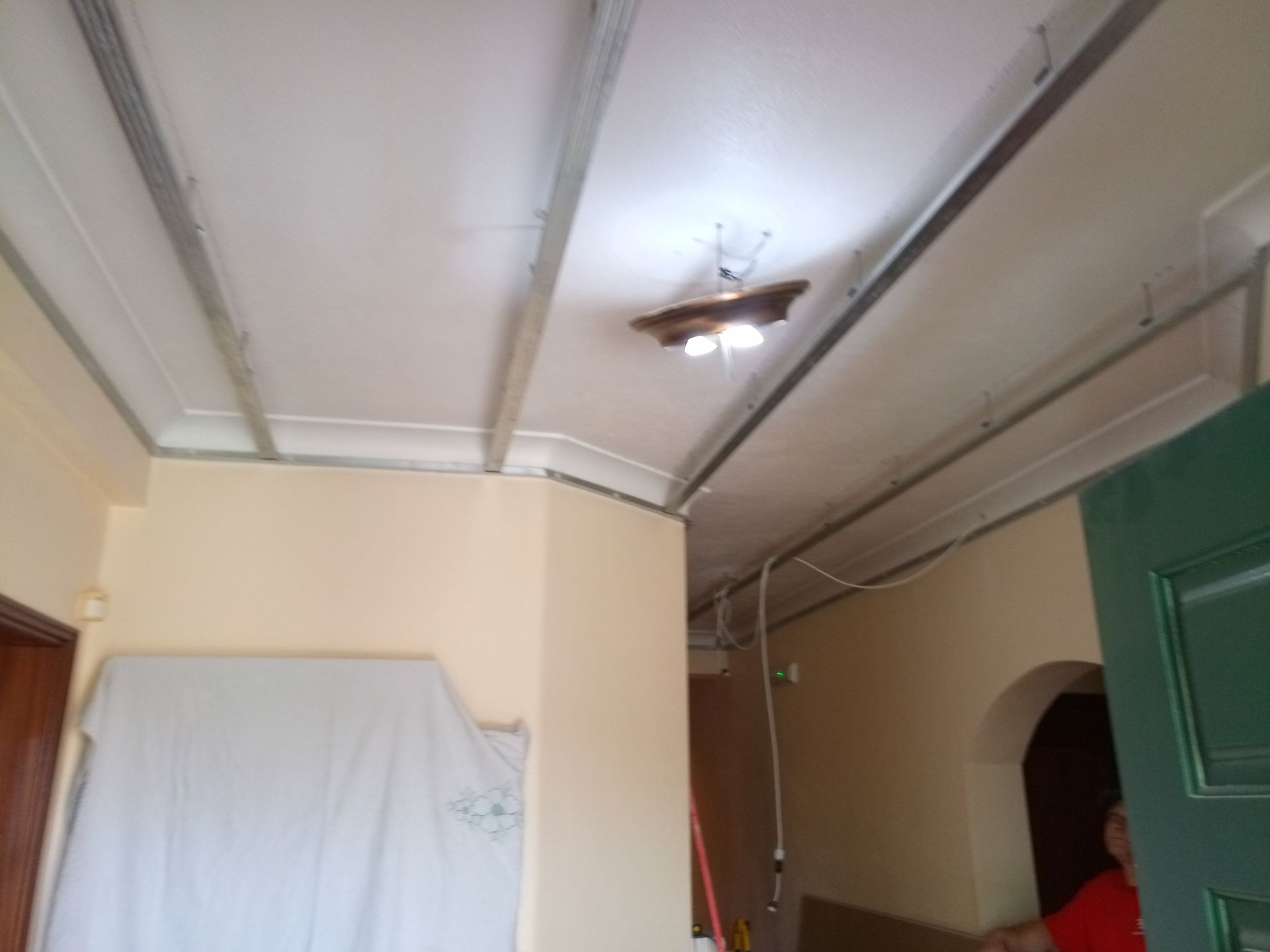 Teto branco com vigas metálicas e luminária, corredor com paredes bege, porta e objeto coberto.