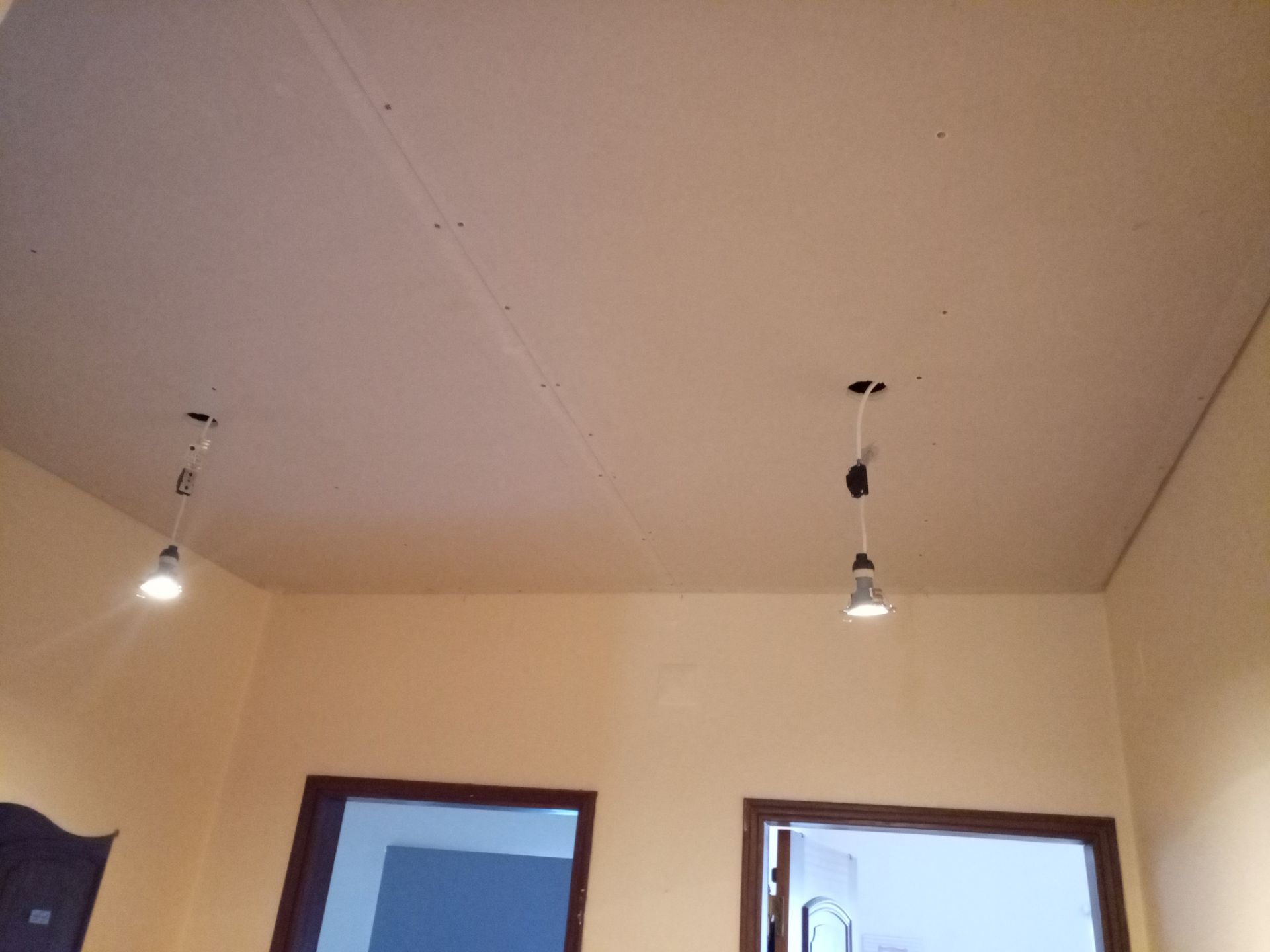 Duas luminárias pendentes suspensas em um teto bege em uma sala com paredes amarelo-claras e duas aberturas com molduras escuras.