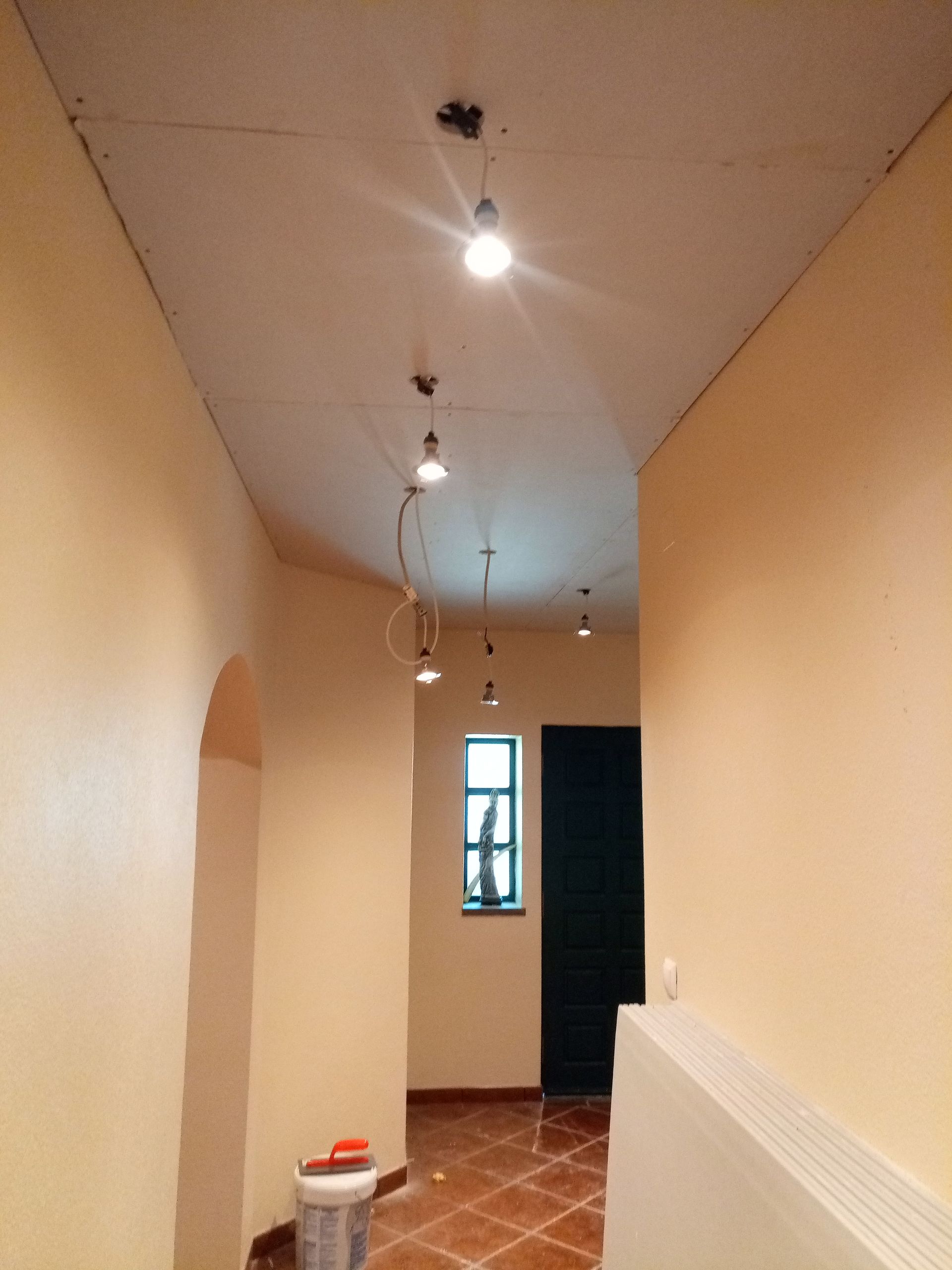 Corredor comprido com luminárias pendentes, paredes cor de pêssego, piso de azulejo, porta preta e janela.