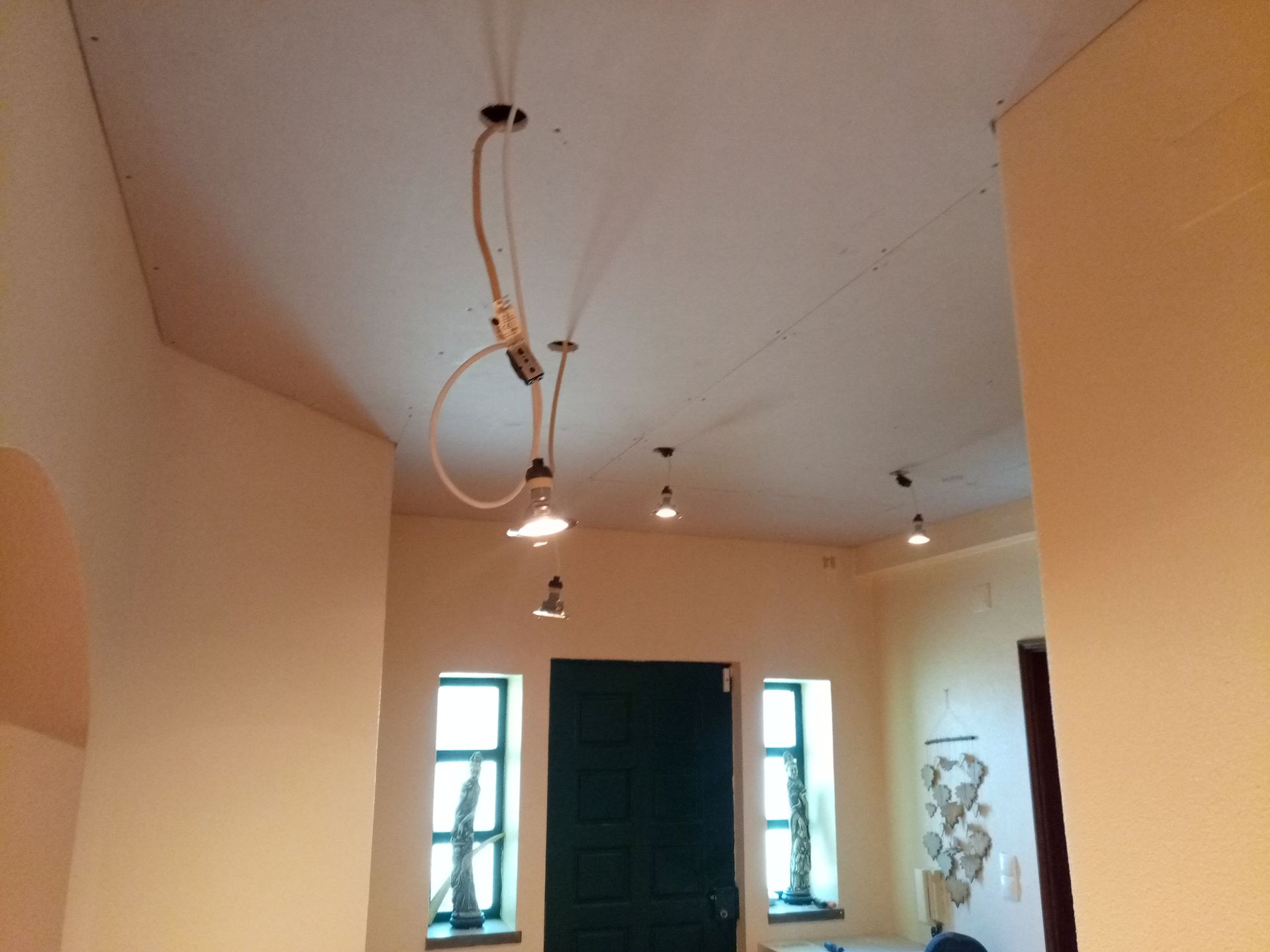 Corredor com paredes e teto em tons creme. Diversas luminárias pendentes. Uma porta escura e janelas são visíveis.