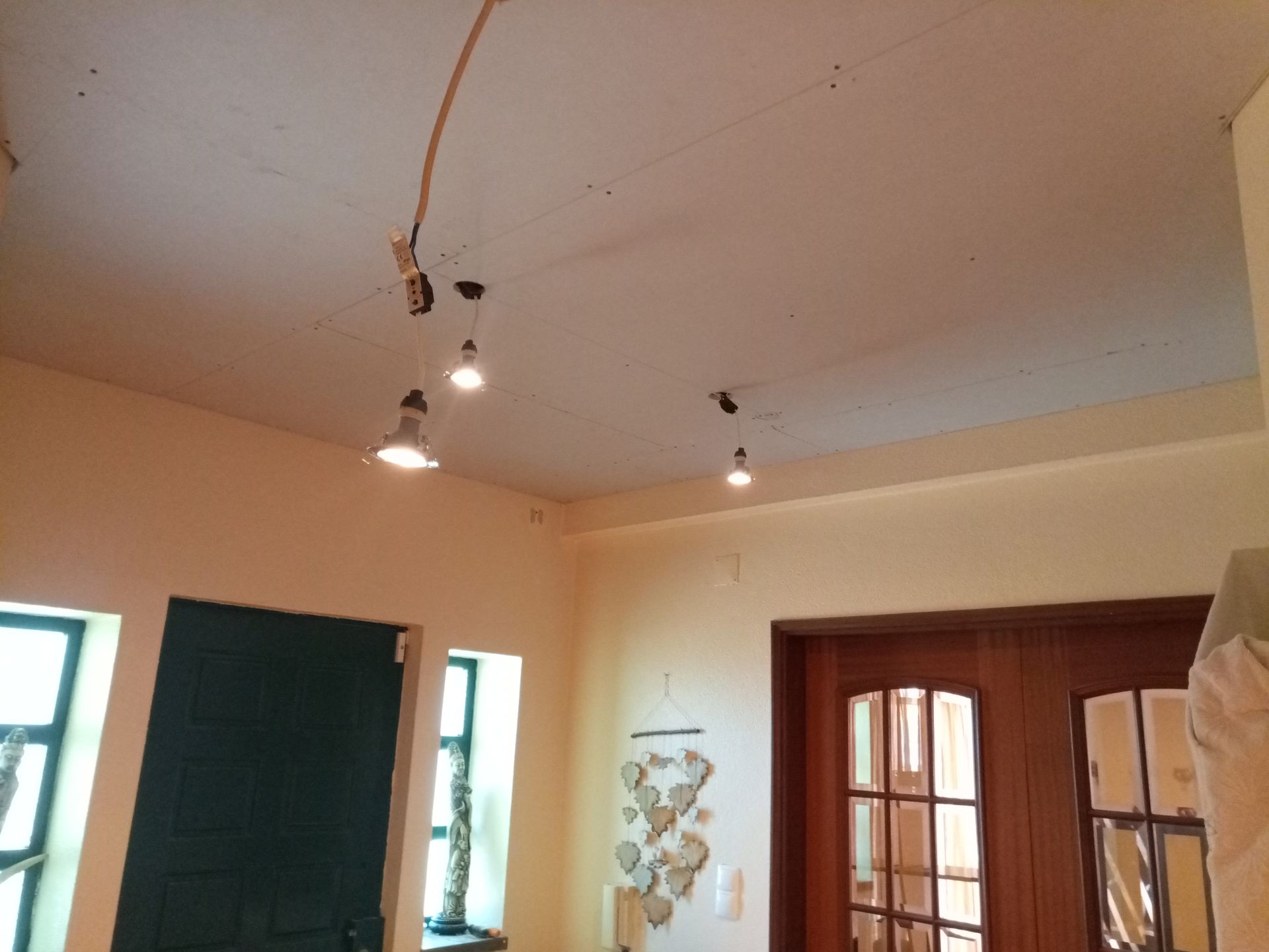 Quarto em tons creme com iluminação em trilho no teto. Portas e janelas visíveis.