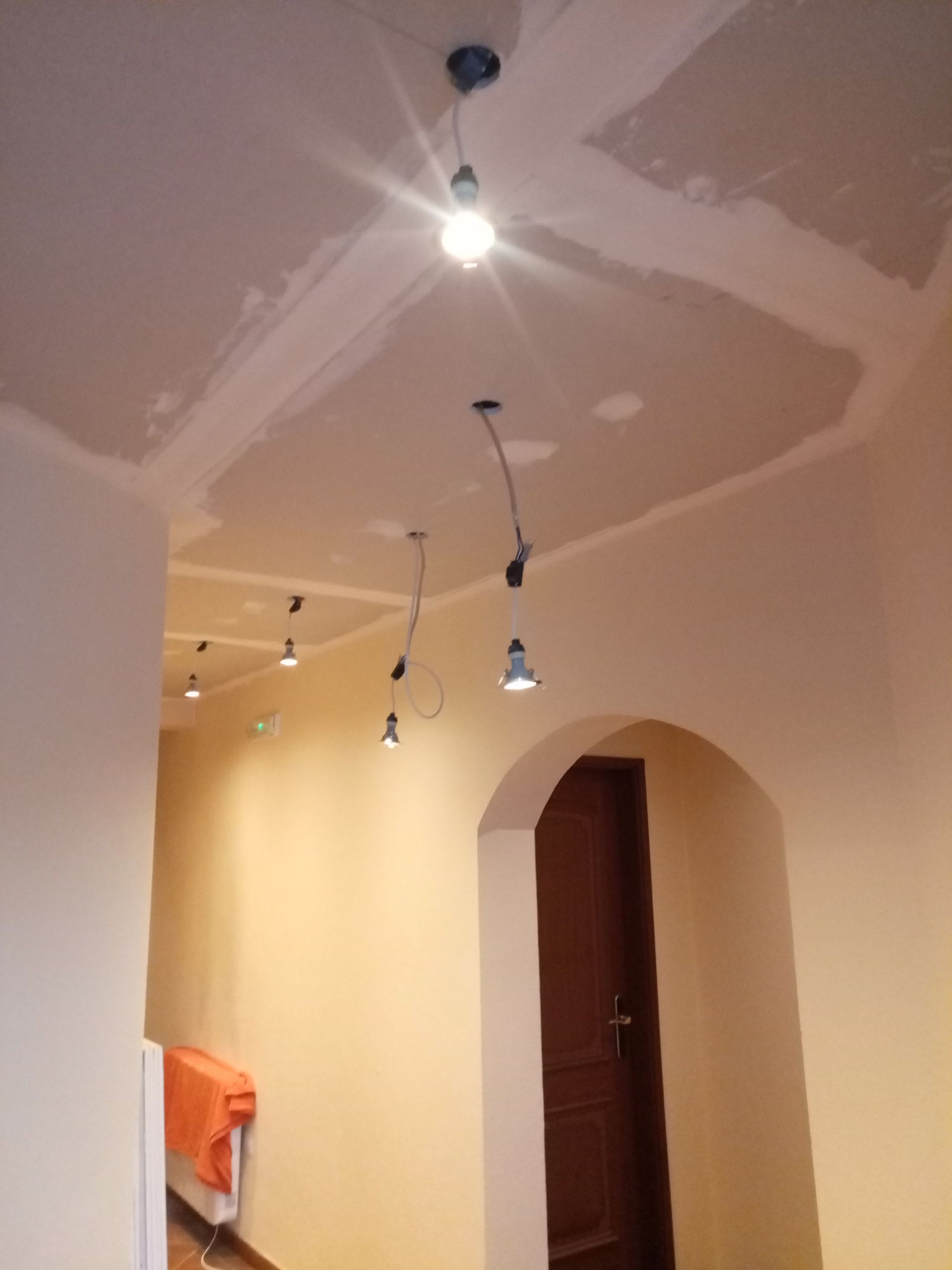 Corredor com luminárias no teto. Porta em arco, porta marrom e paredes cor de pêssego.