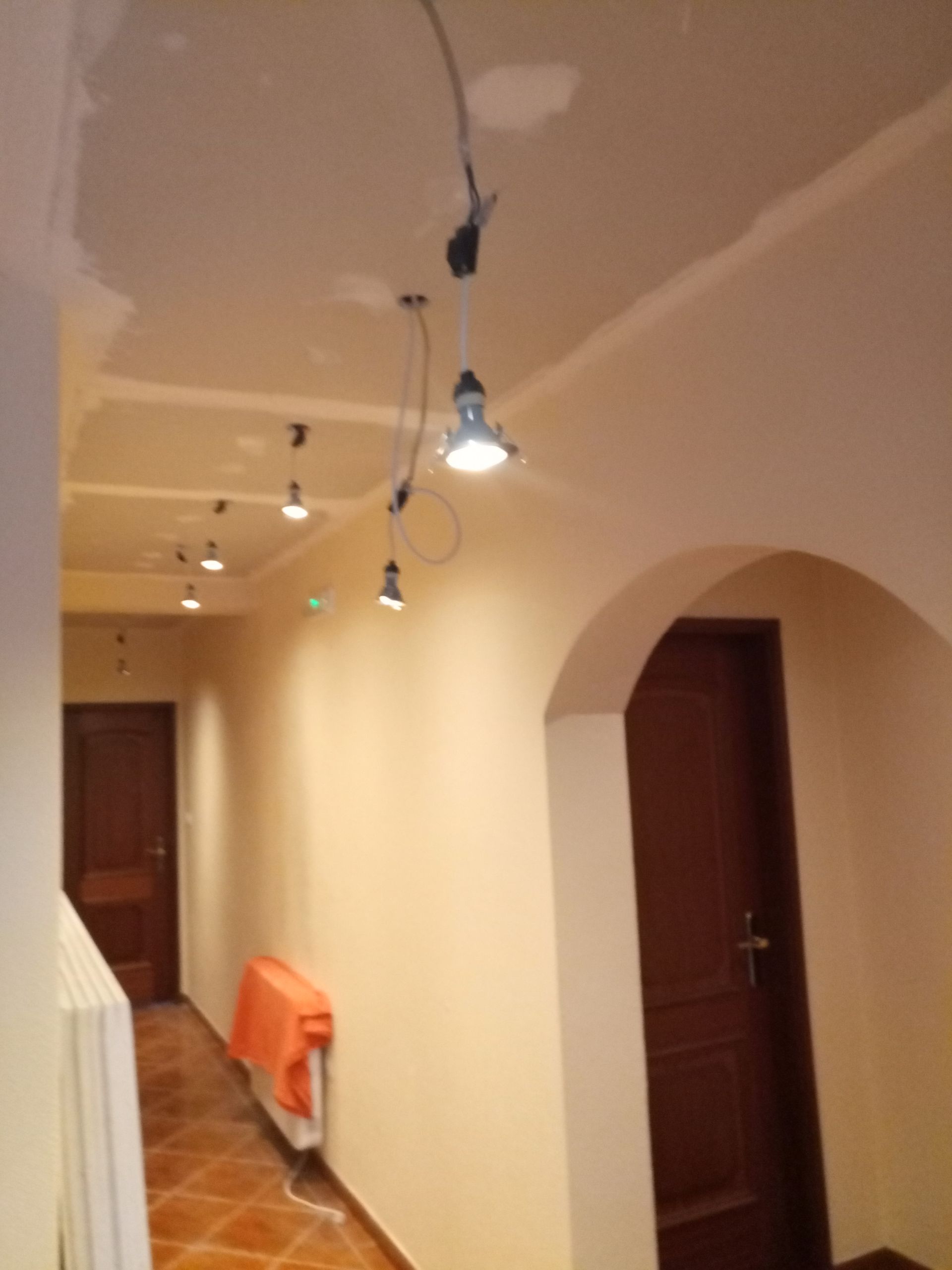 Corredor com iluminação embutida no teto; paredes bege, portas marrons, piso de azulejo.