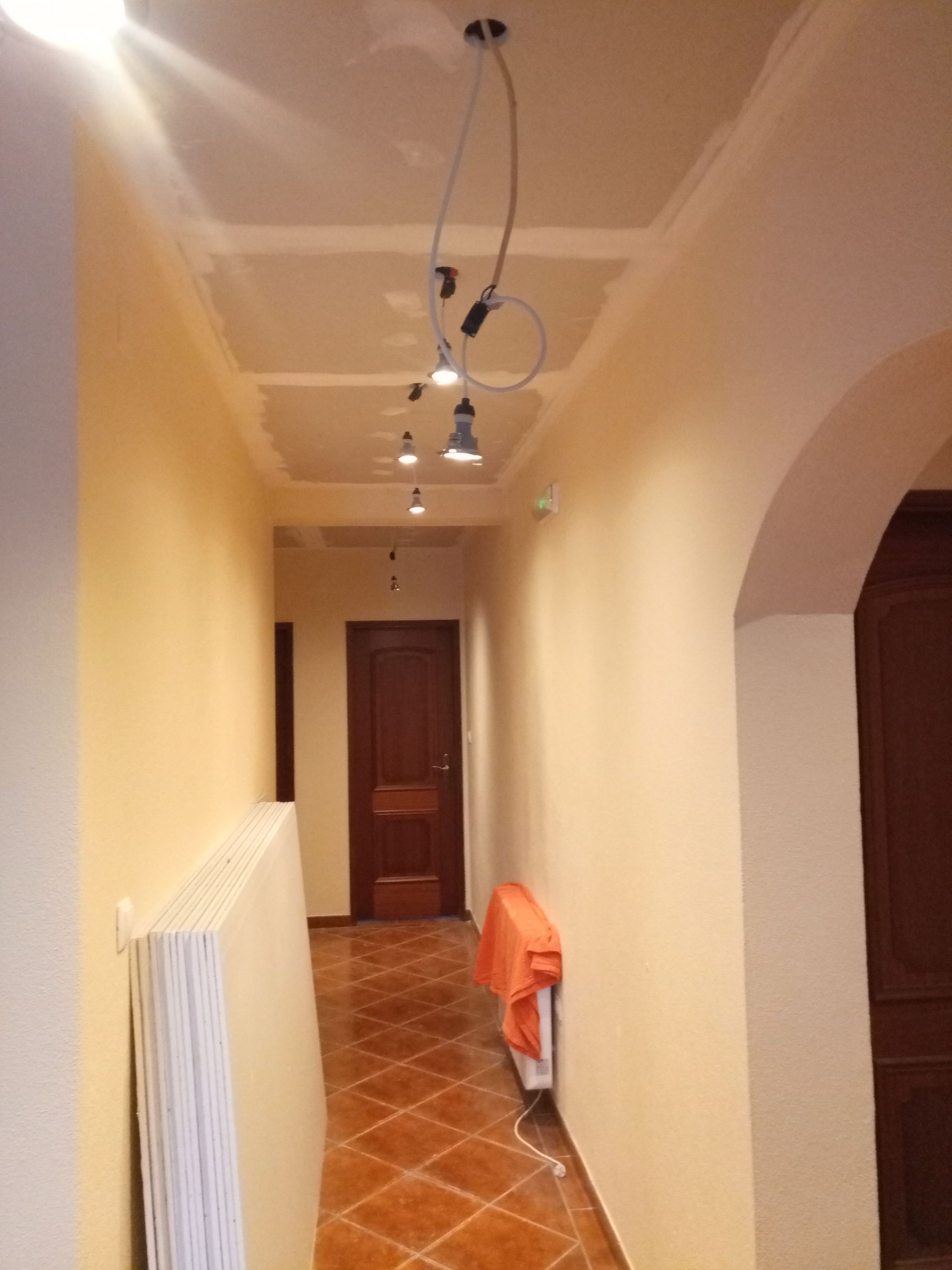 Corredor com iluminação, radiador e porta em arco, paredes em tons neutros e piso de azulejo.