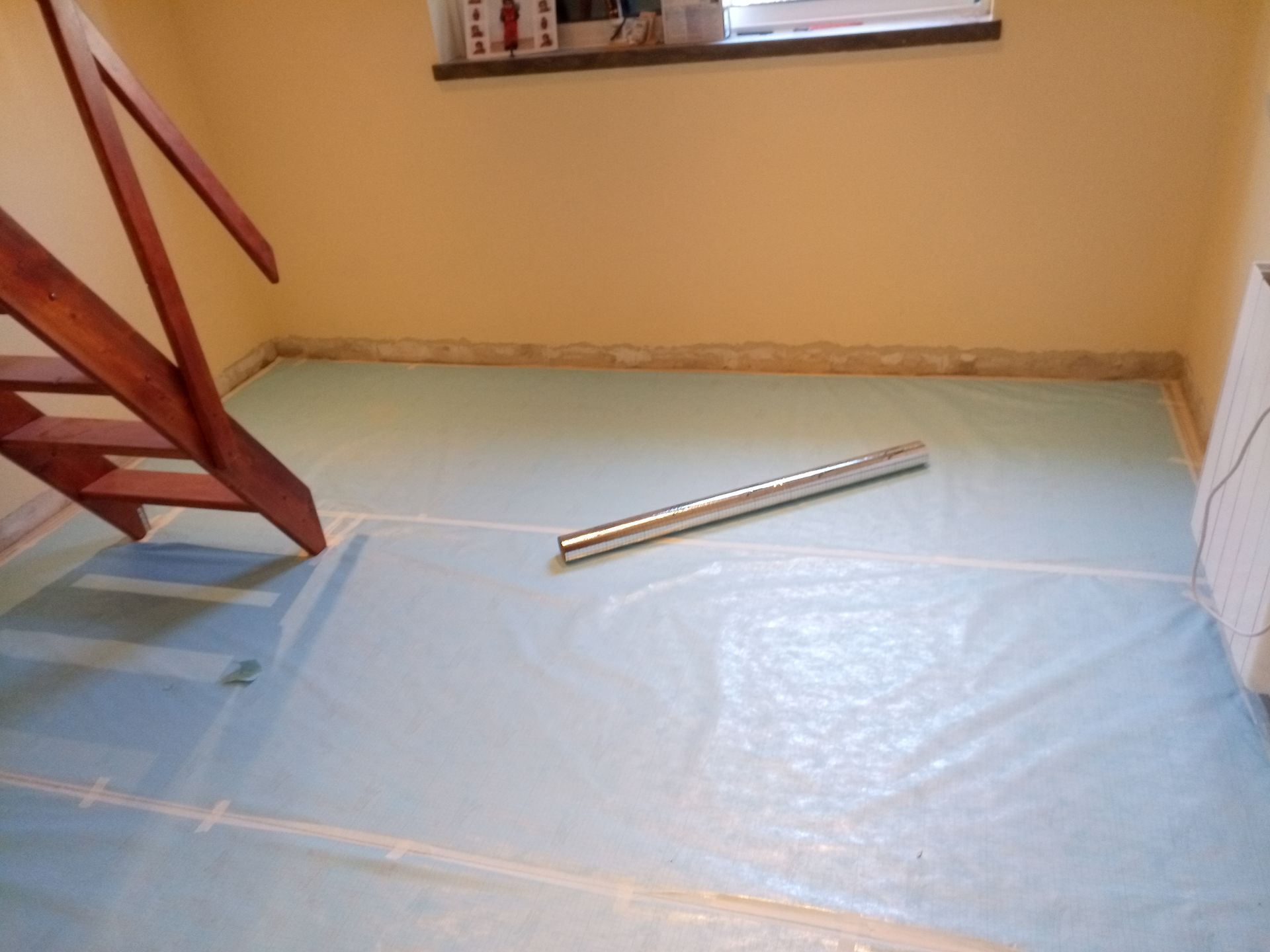 Quarto com escada de madeira, piso azul coberto com lona plástica, plano e paredes bege.